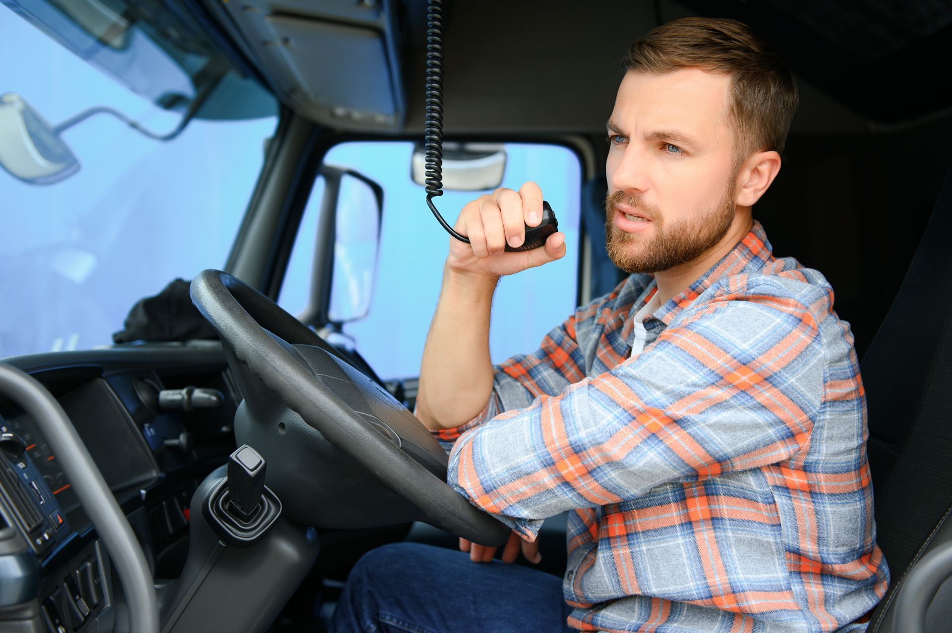 a man is sitting in the driver 's seat of a truck talking on a walkie talkie .