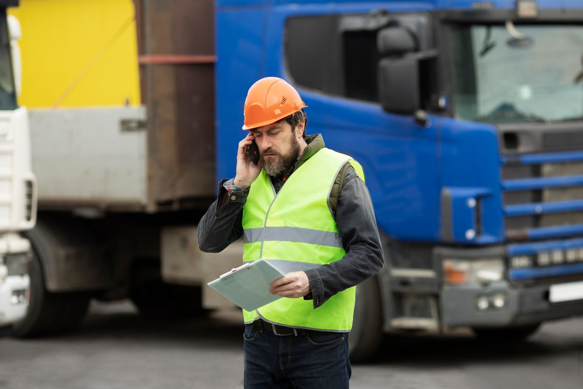 a man is talking on a cell phone while holding a clipboard in front of a truck .