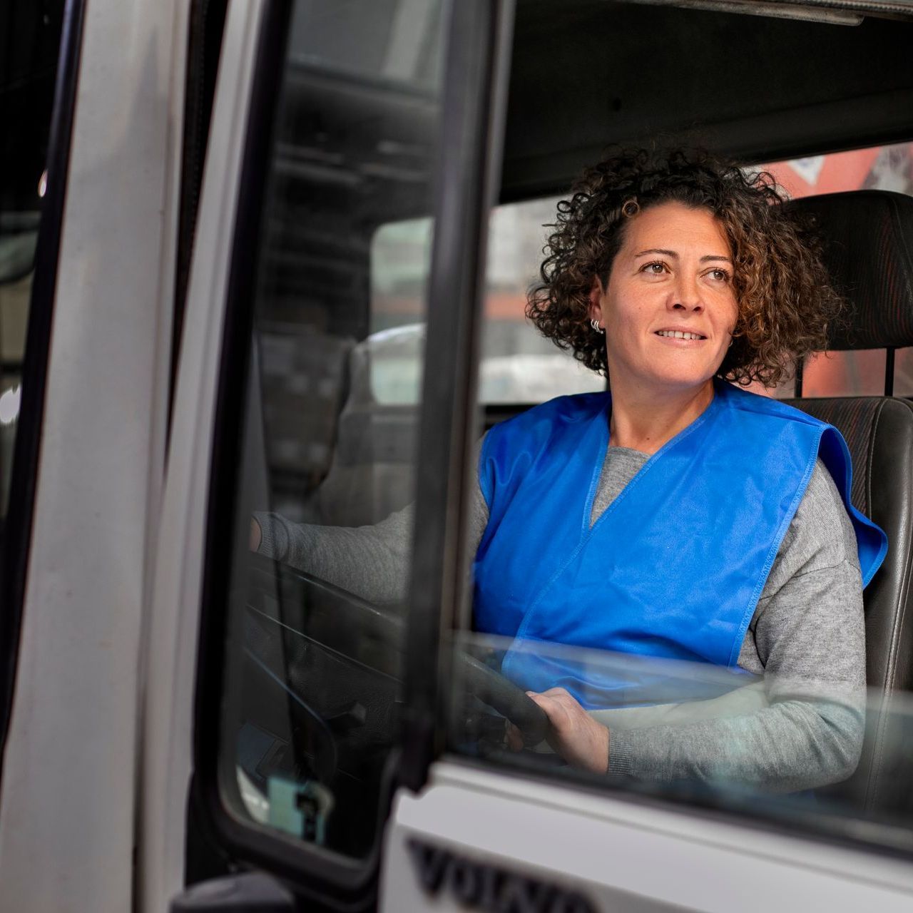 a woman in a blue vest is driving a volvo truck