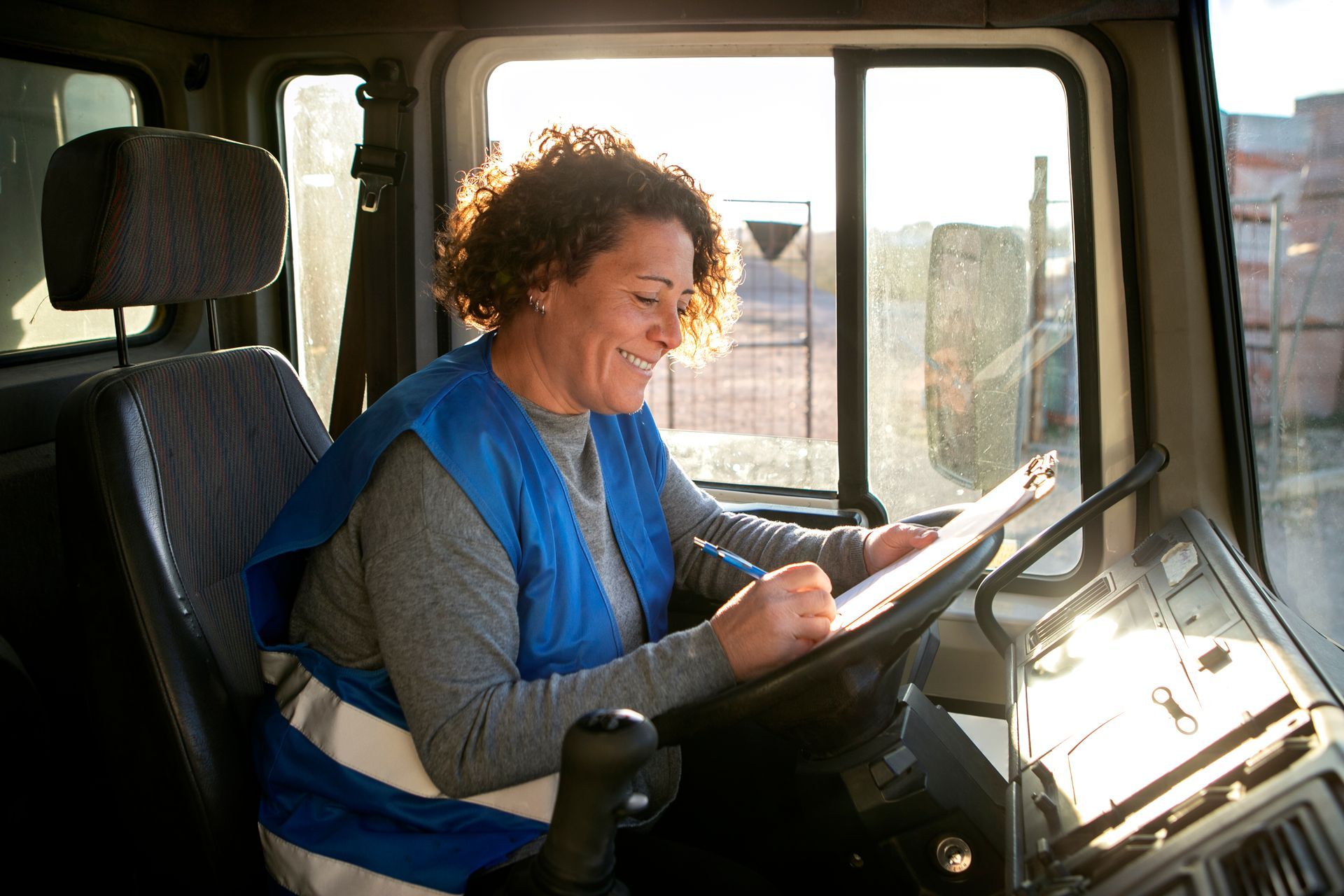 a woman is sitting in the driver 's seat of a truck looking at a clipboard .