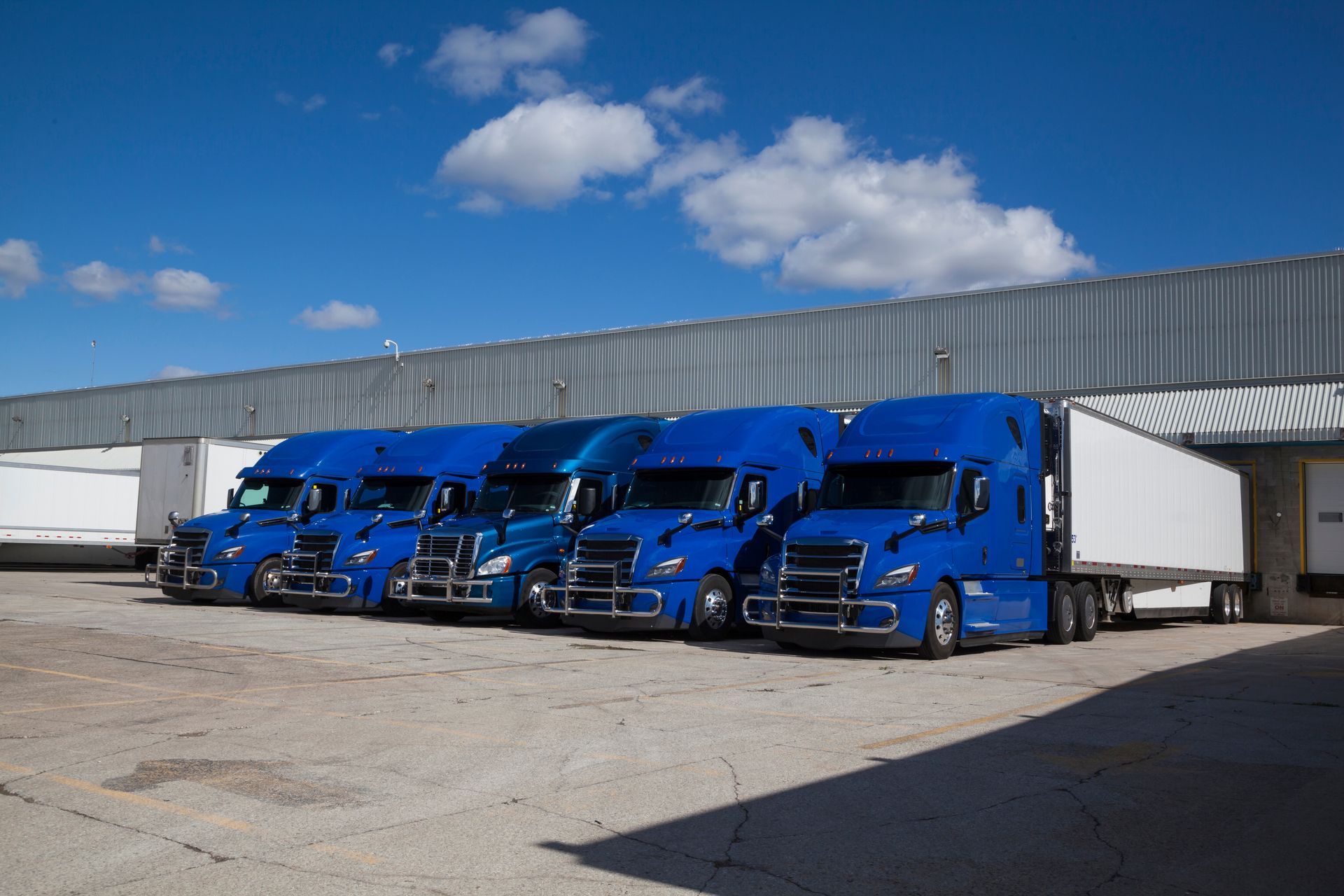 a row of blue semi trucks parked in front of a building .