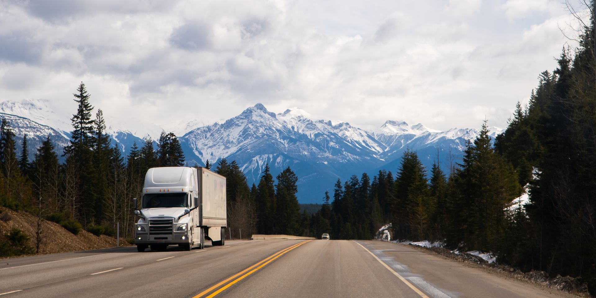 a semi truck is driving down a highway with mountains in the background .