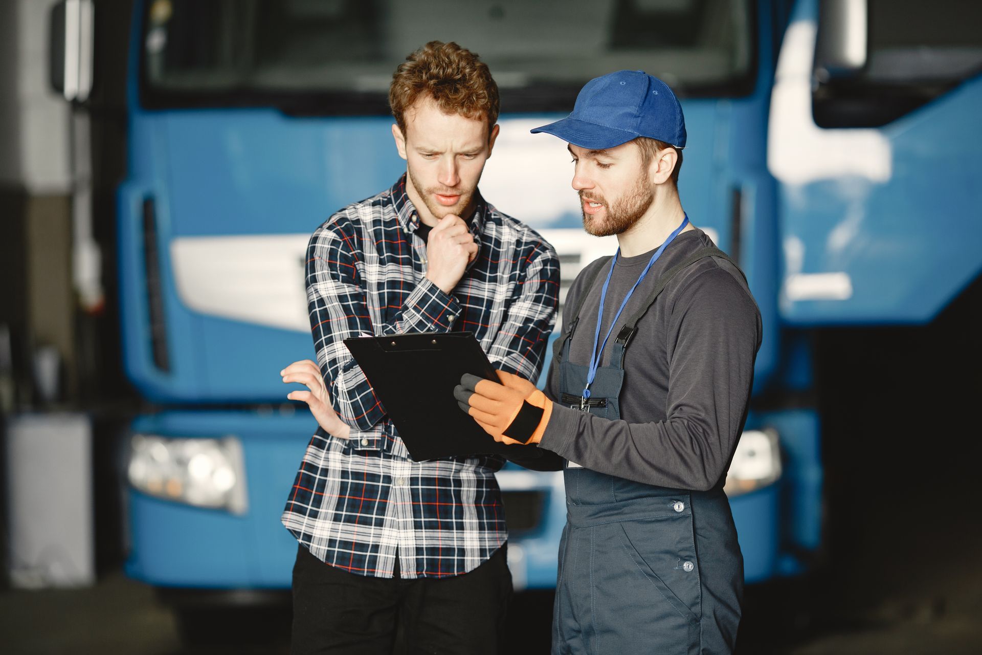 two men are standing in front of a blue truck looking at a clipboard .