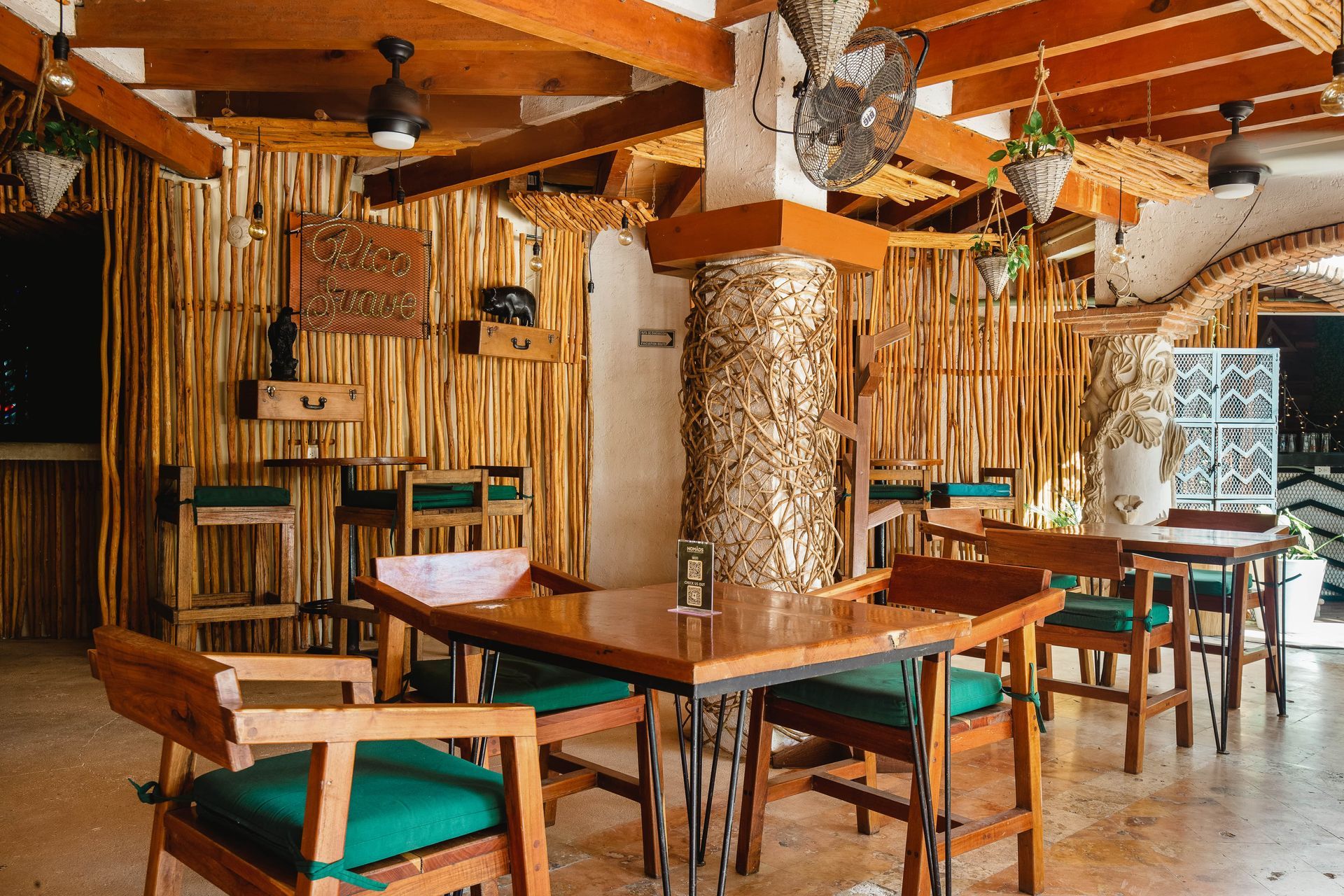 A restaurant with wooden tables and chairs and a bamboo wall.