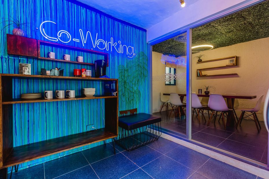 A room with tables and chairs and a neon sign that says coworking.