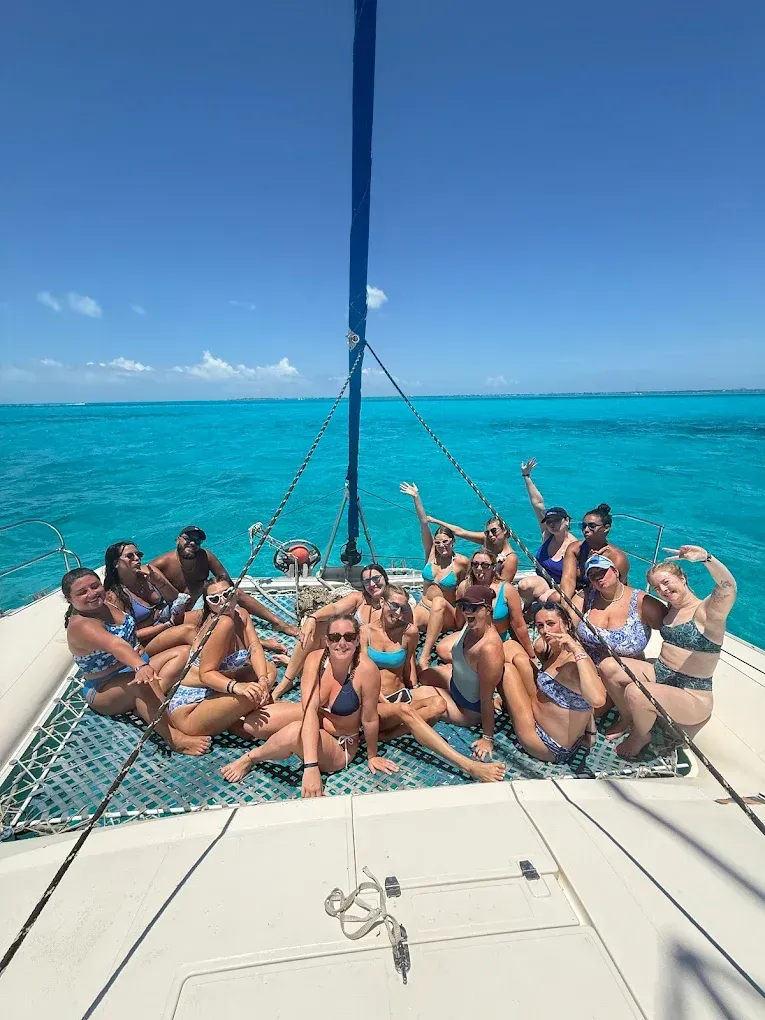 Group of people in swimwear on a catamaran, posing in the turquoise ocean under a blue sky.