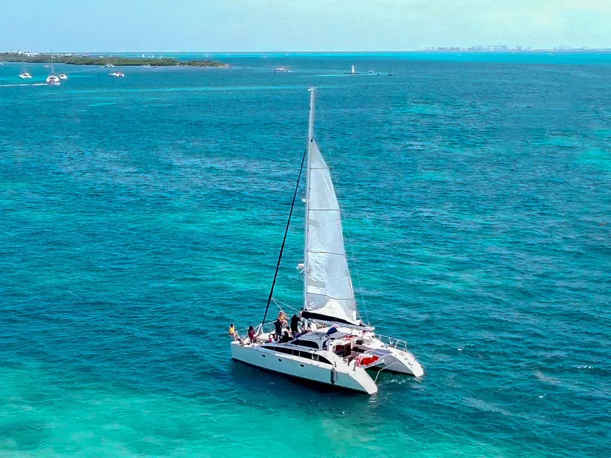 Catamaran sailing on turquoise water; white sails, blue sky.