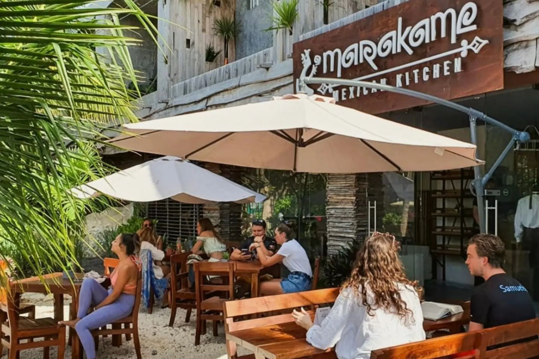 A group of people are sitting at tables under umbrellas in front of a restaurant.