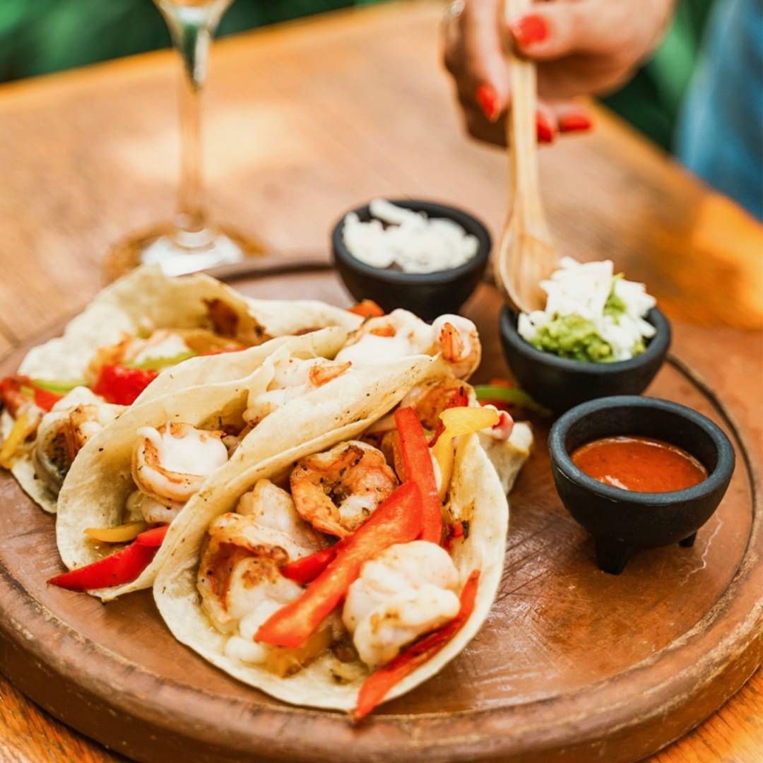 A person is cutting a taco with a spoon on a wooden cutting board.