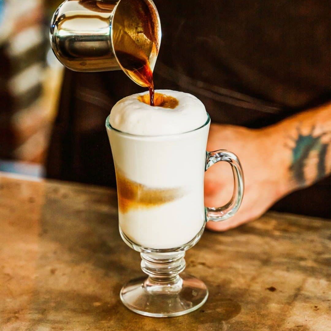 A person is pouring coffee into a glass of milk