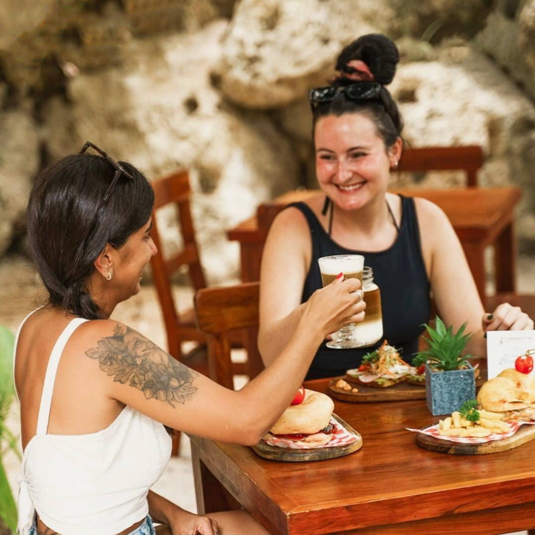 Two women are sitting at a table with food and drinks