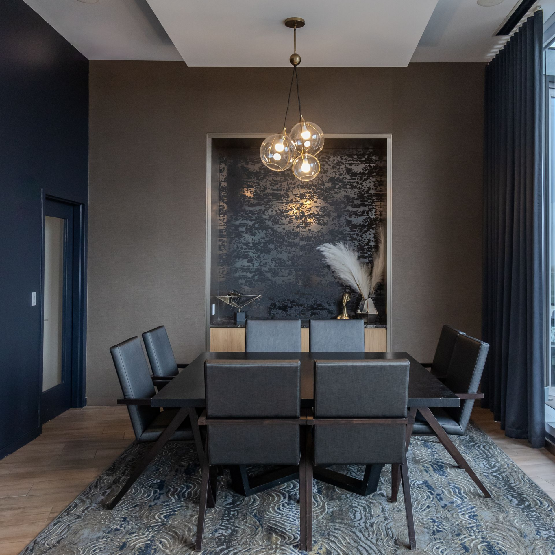 Dining room with dark furniture, blue rug, and decorative pendant lights.