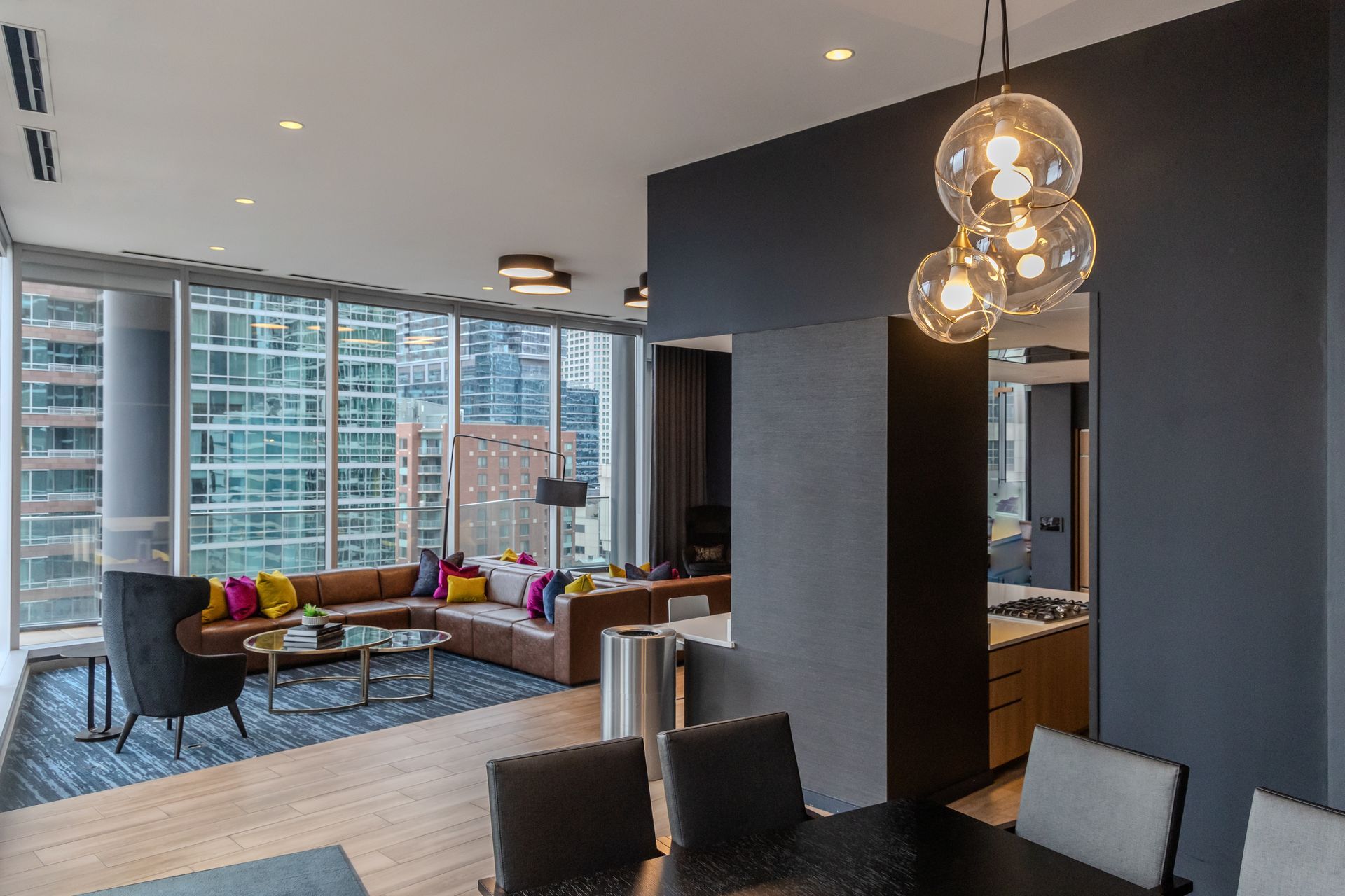 Modern living room with city view, leather sectional, dark accent wall, and glass globe light fixture.