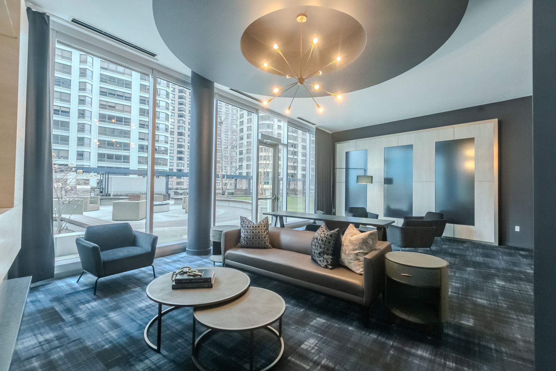 Modern lounge with seating, coffee tables, large windows, and a chandelier.