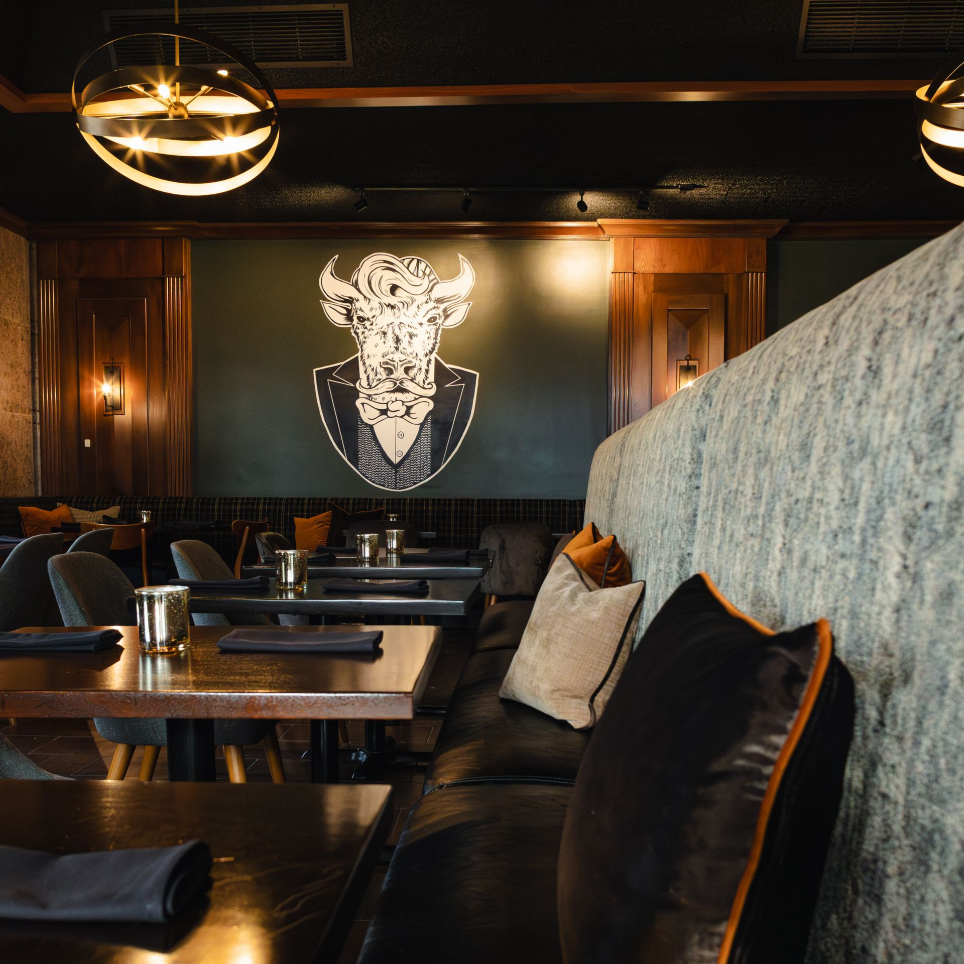 Dark restaurant interior with booths, tables, and a bull head art piece.