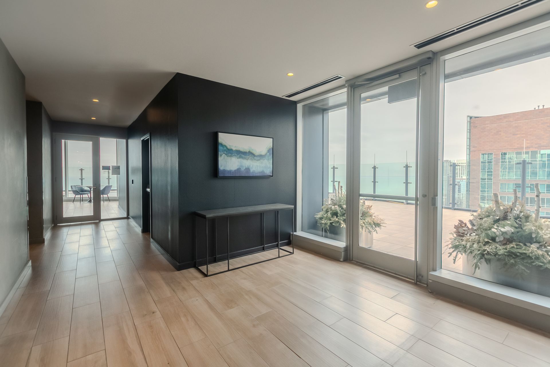 Modern condo hallway with wood floors, black accent wall, and large windows leading to a balcony.
