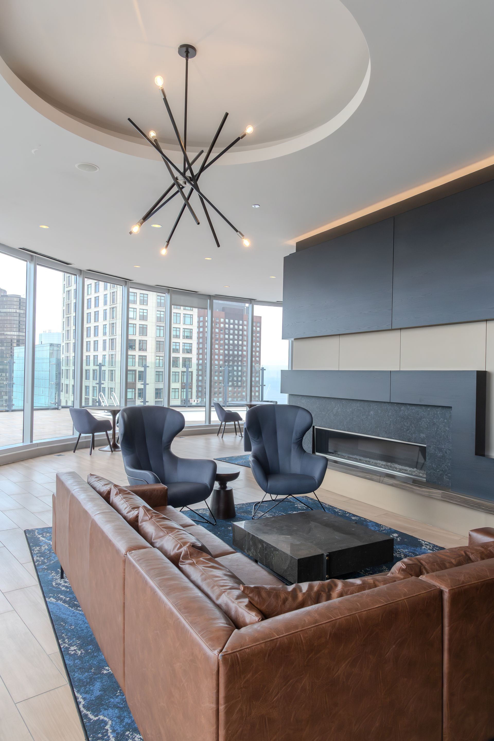 Modern living room with leather sofa, blue chairs, fireplace, and city view.