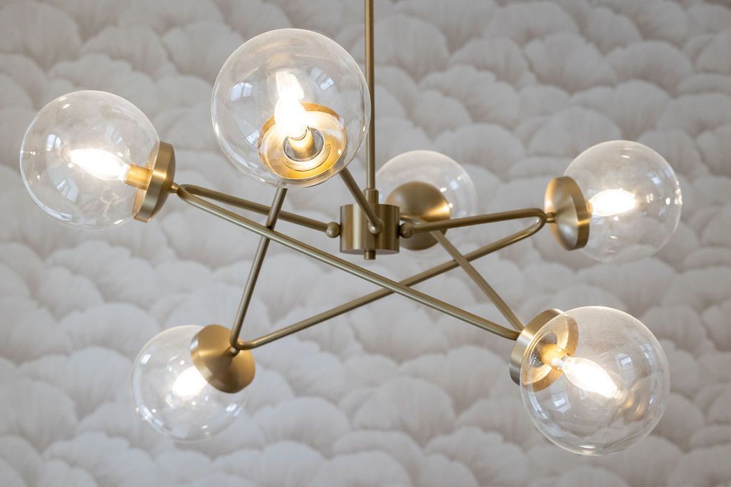 Gold and glass orb chandelier with six lights, against a textured white wall.