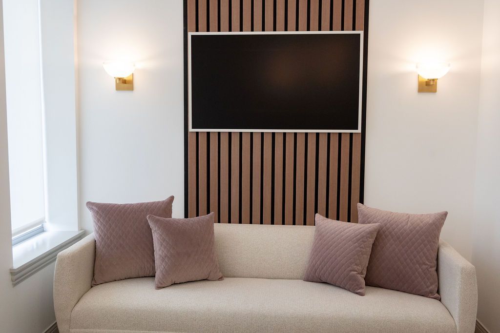A living room with a cream sofa and four pink pillows, a mounted TV, and wood paneling on the wall.