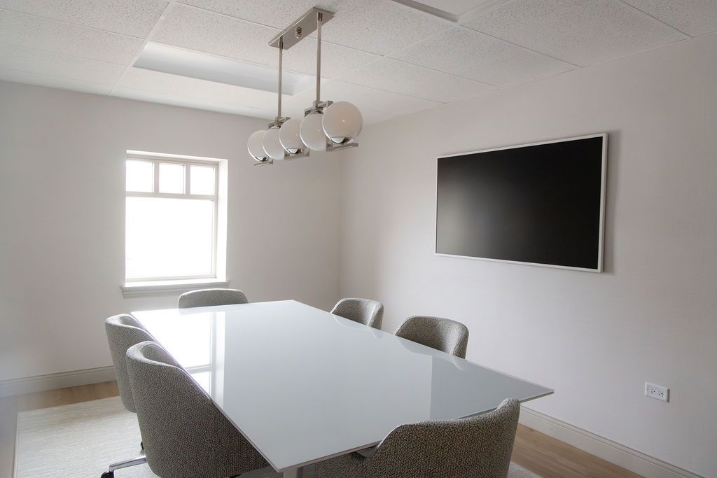 Conference room with a rectangular glass table, chairs, TV, window, and pendant lights.