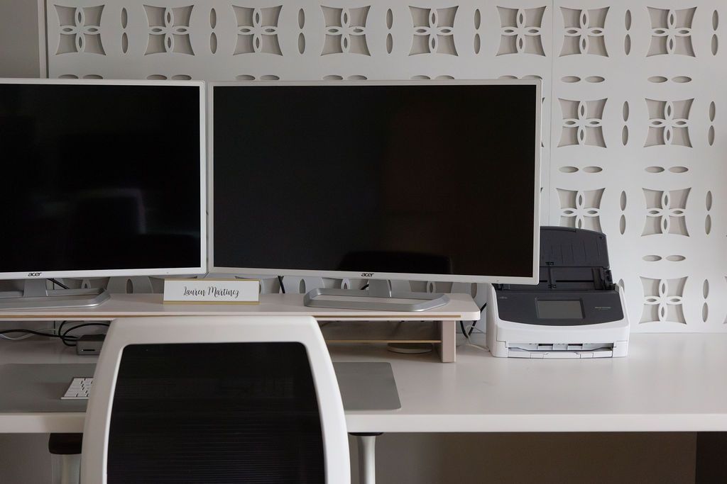 Desk with two monitors, white chair, and decorative patterned wall. Printer on the desk.