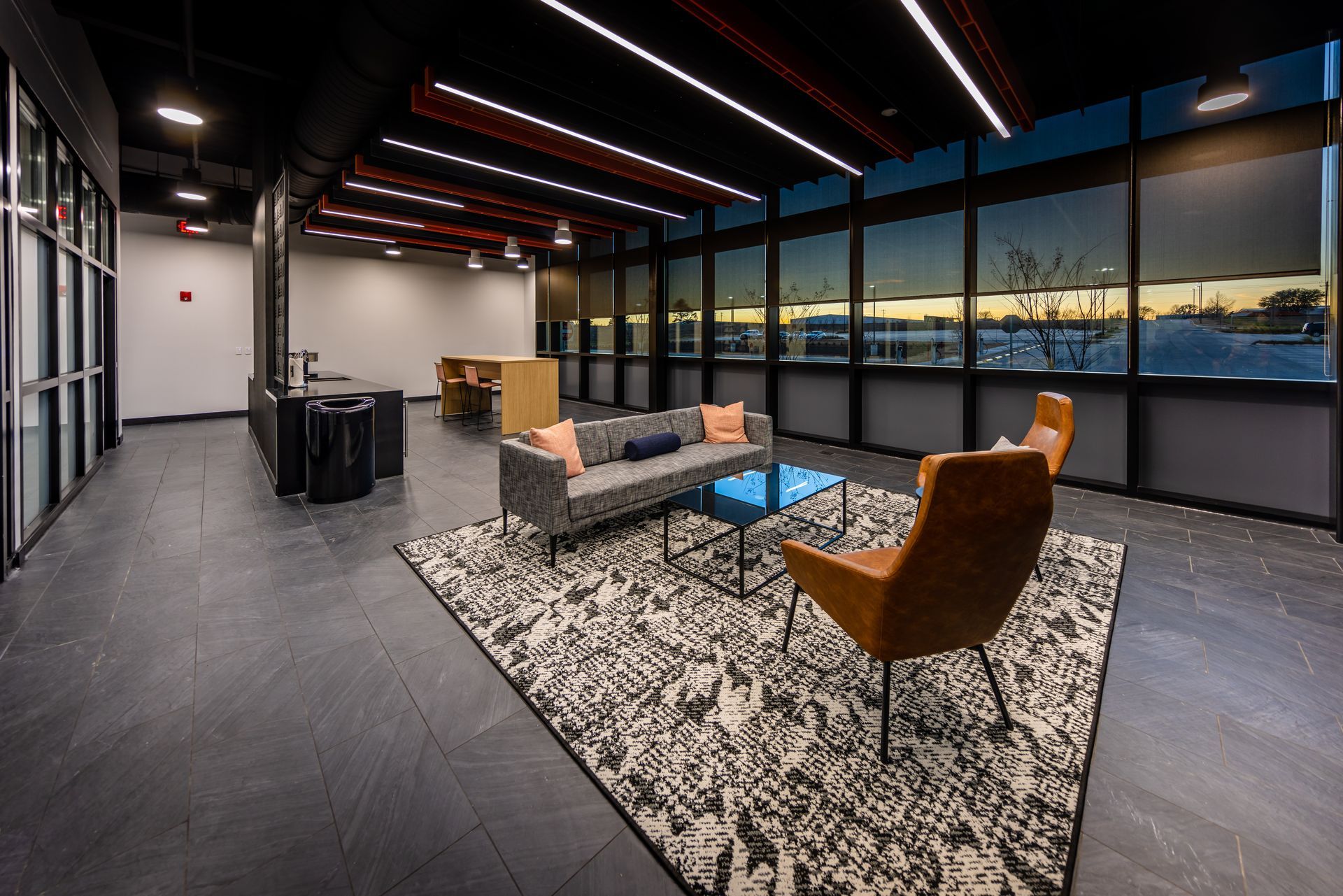 Modern office lounge with seating, patterned rug, and large windows overlooking snow.