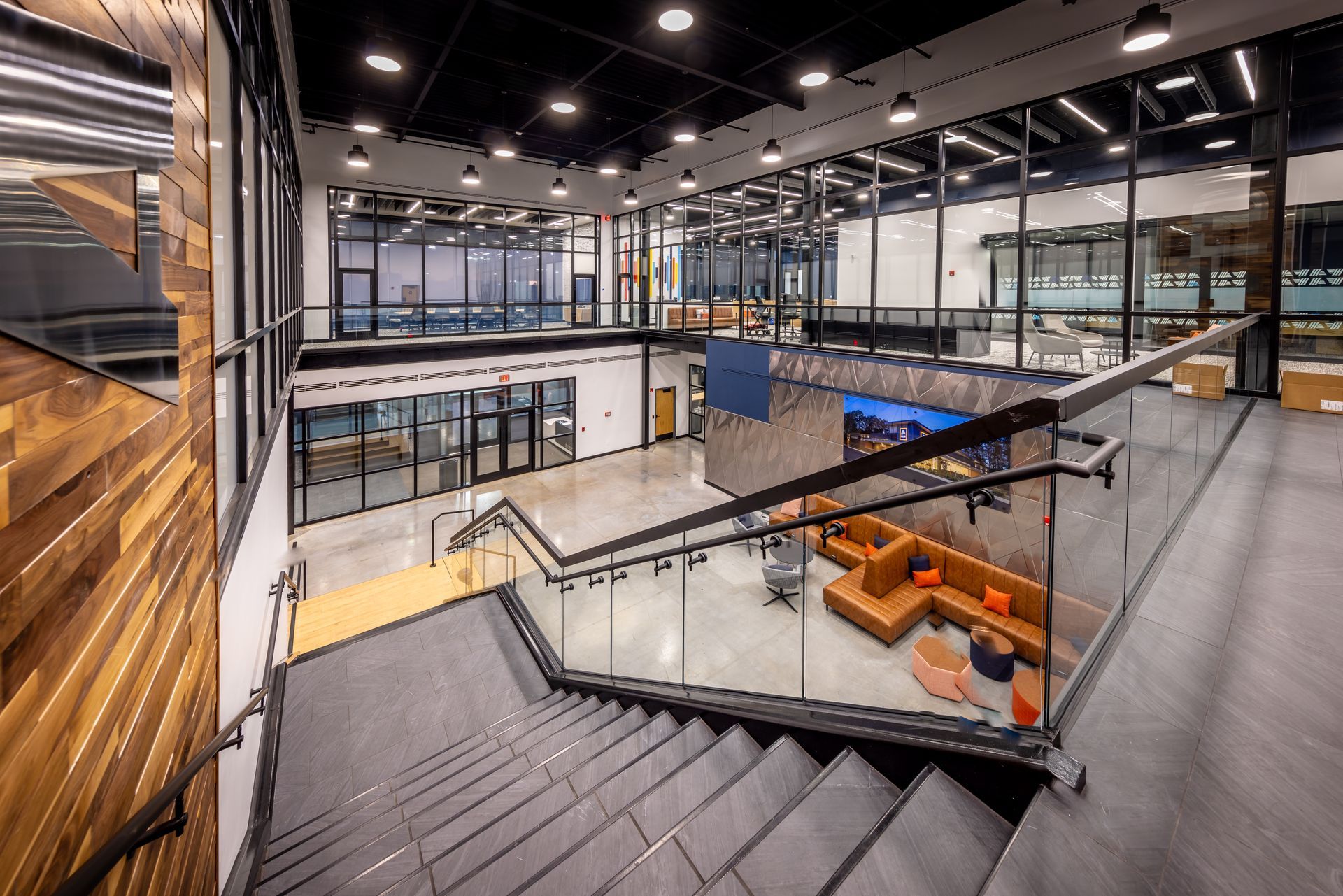 Modern office interior with staircase, multiple levels, and glass walls.  Orange seating and wood accents are visible.