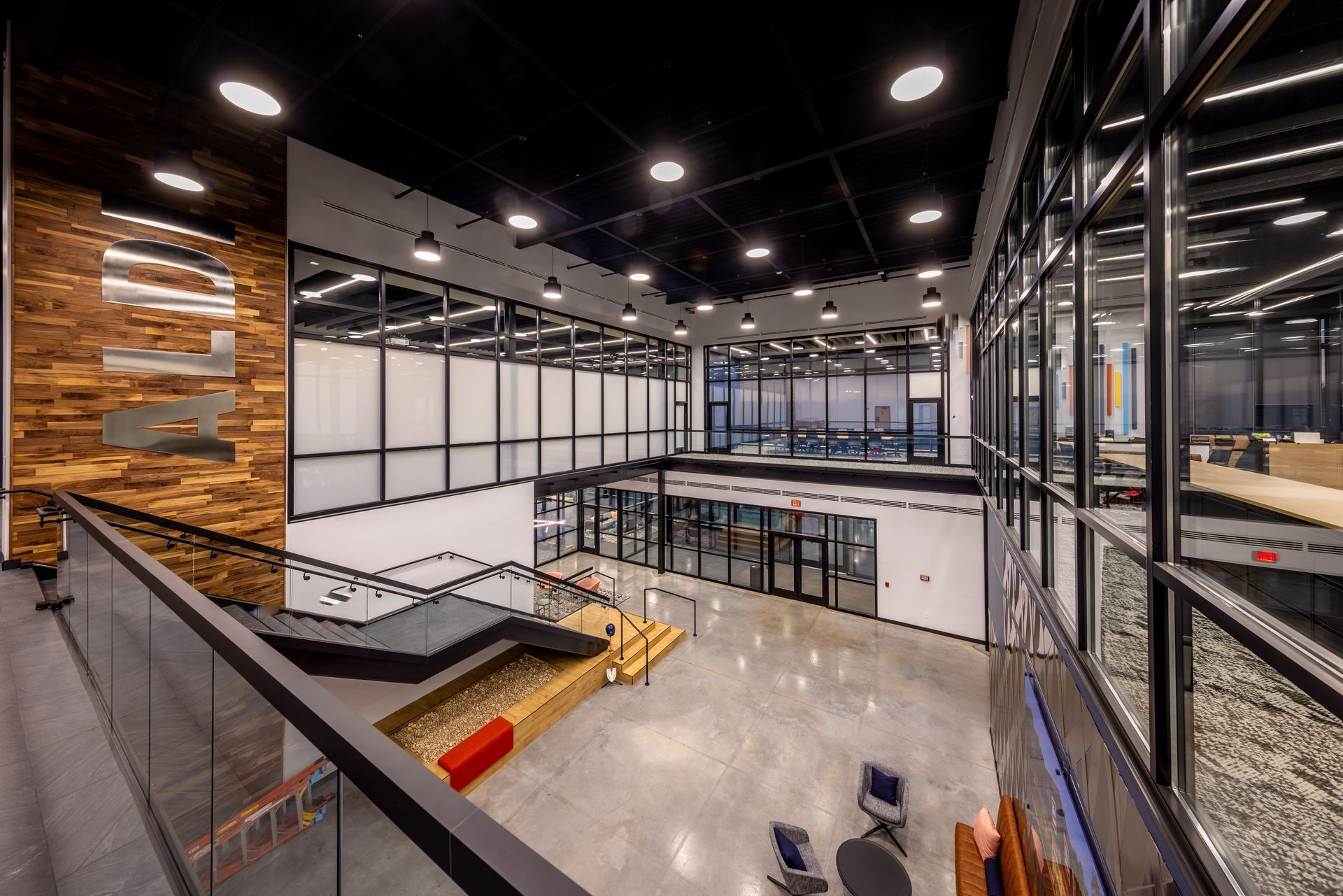 Modern, multi-level office interior with glass walls, concrete floors, and a wooden accent wall.