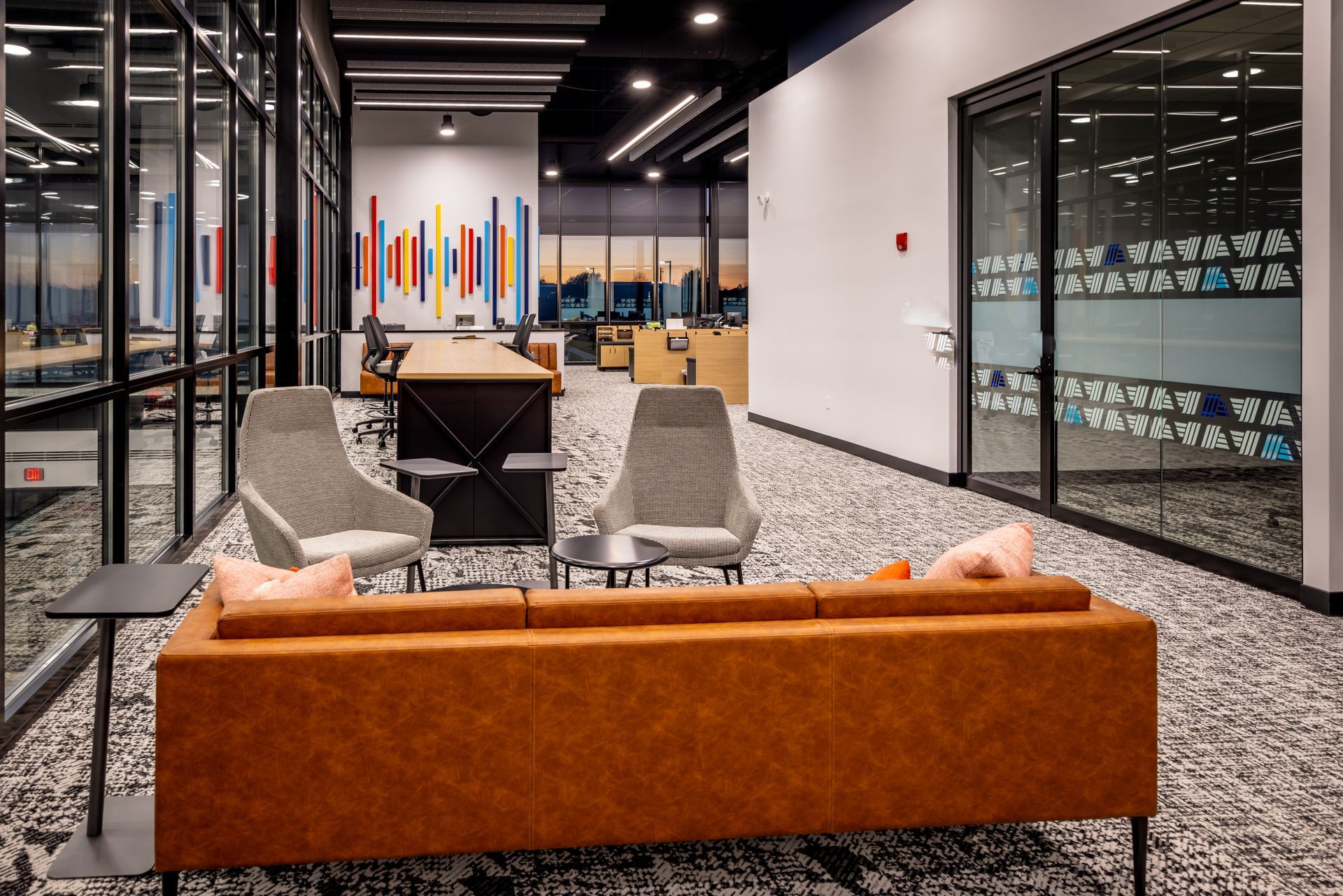 Modern office lounge area with seating, glass walls, and abstract artwork.