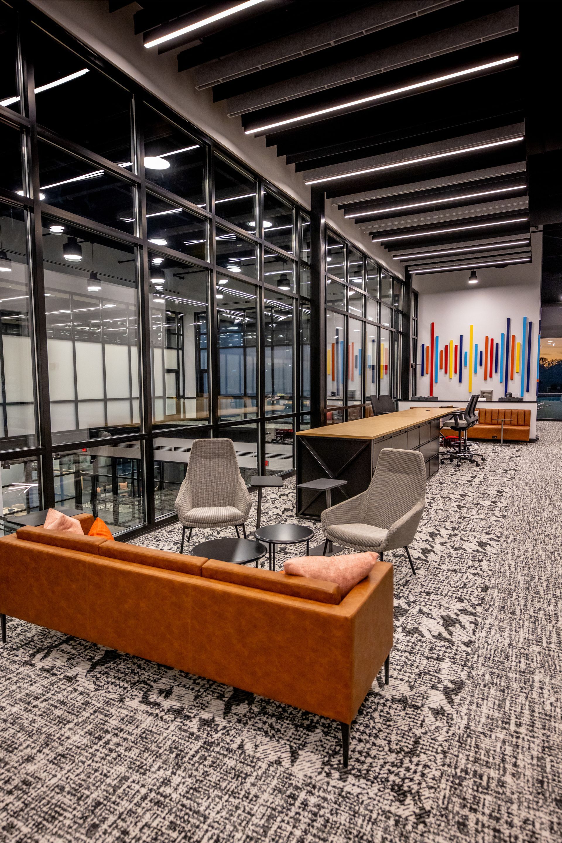 Modern office lounge with a long sofa, armchairs, and large windows.