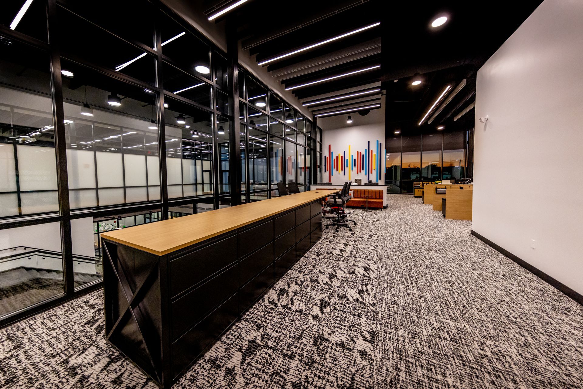 Modern office interior with black and wood details, glass walls, and patterned carpet.