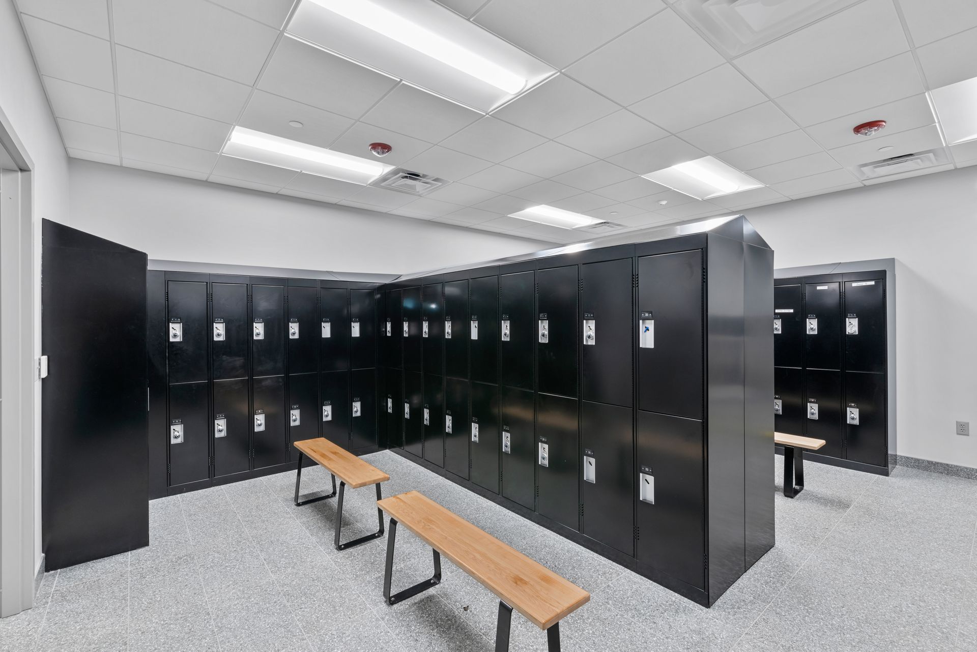Locker room with rows of black lockers, wooden benches, and bright overhead lights.
