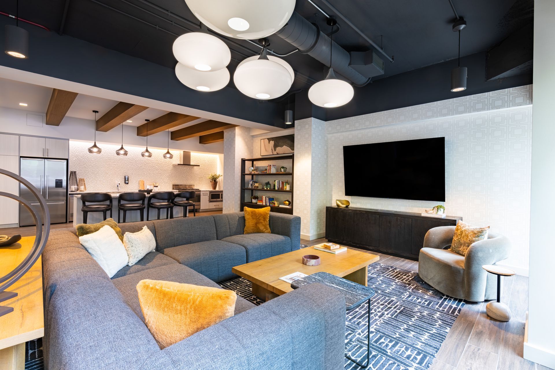 Cozy co-working space: woman walks past seating area with blue armchairs, round table, and high table with laptop.