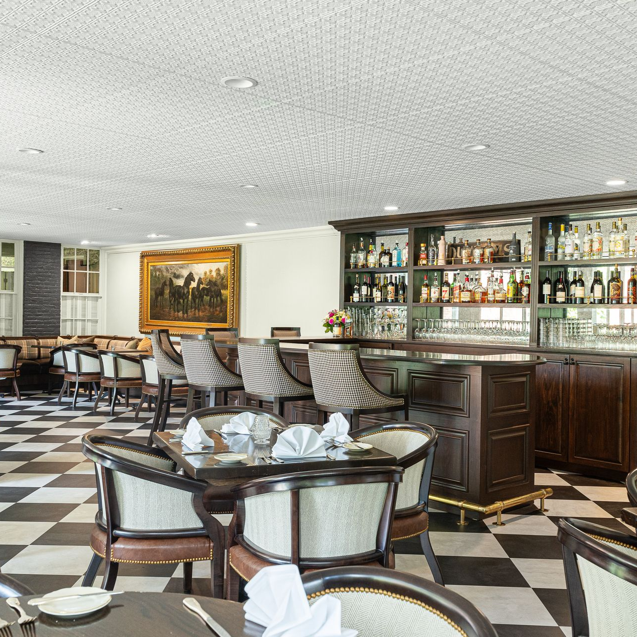 Restaurant interior with checkered floor, bar, and tables with chairs. Artwork on the wall.