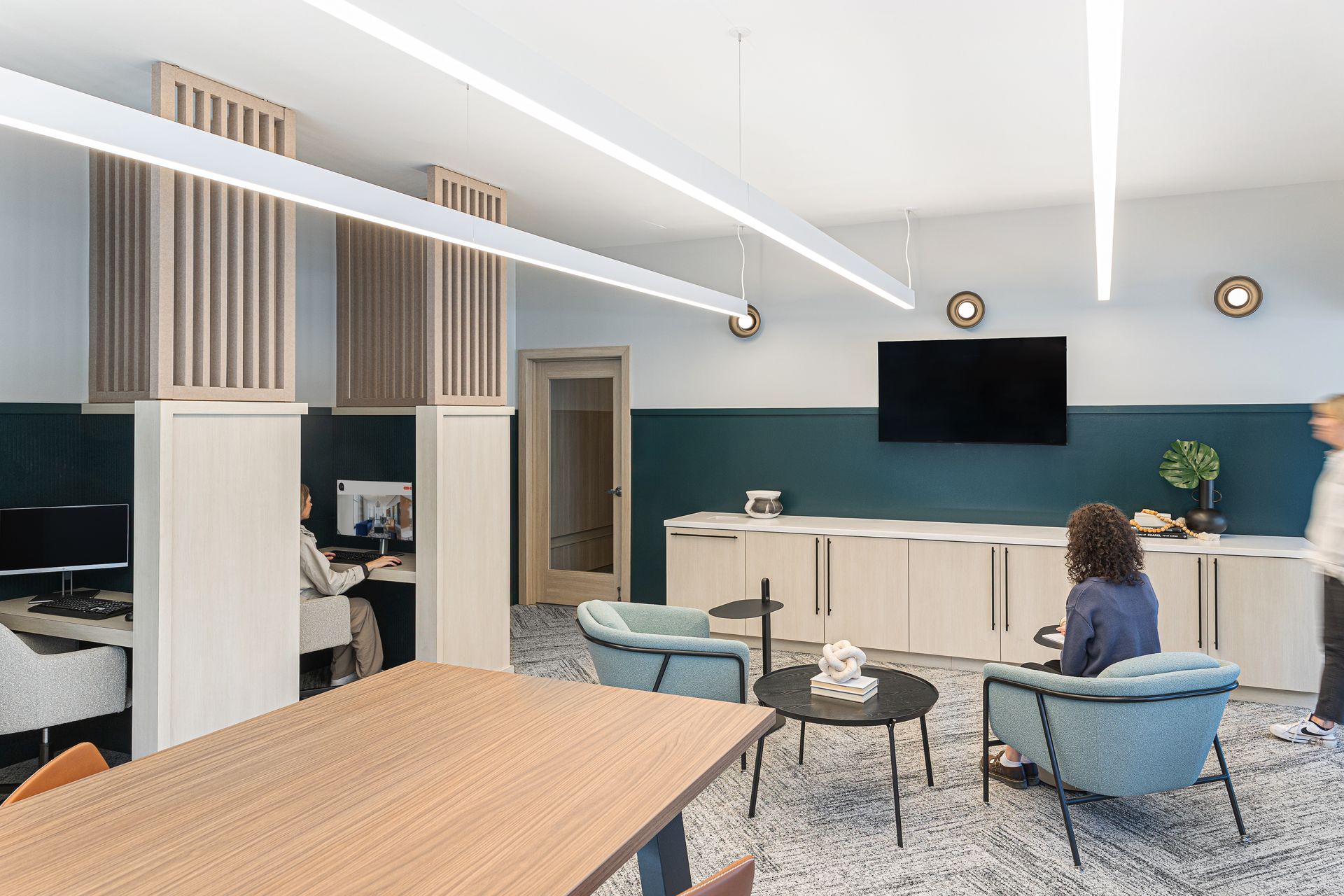 Office space: cubicles, waiting area with blue chairs, TV, and decorative lighting. Two people in the area.