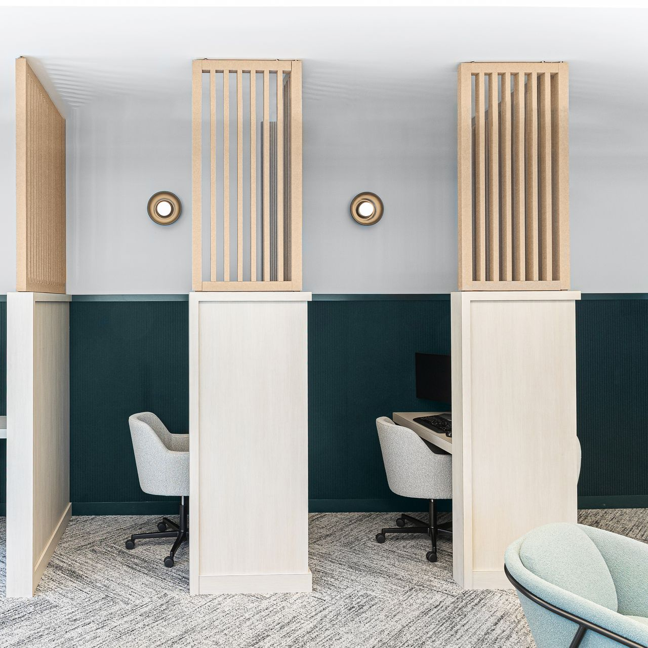 Work cubicles with light wood dividers and decorative wall panels, dark teal and white walls, two office chairs.