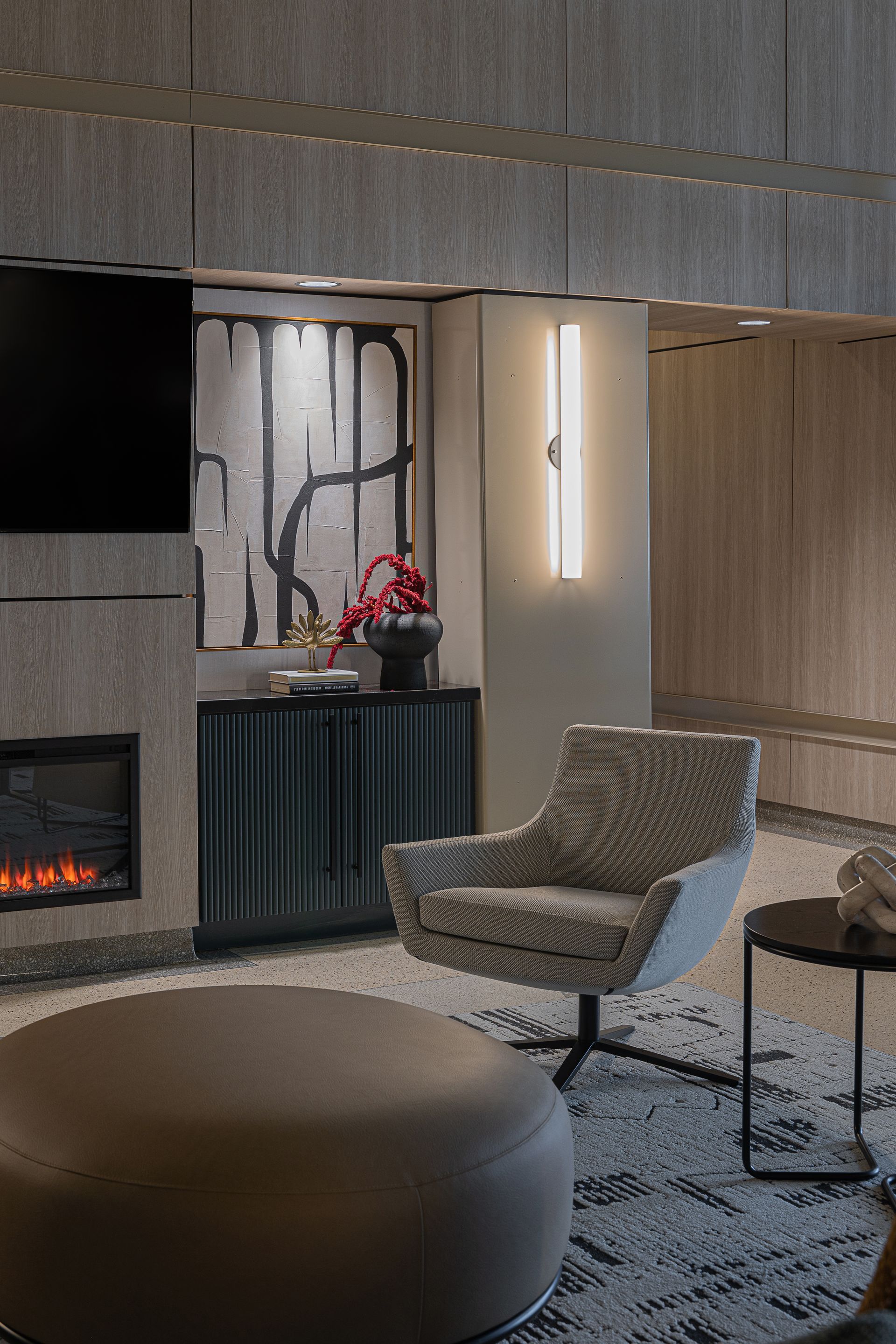 Cozy living room with fireplace, abstract art, modern chair, and ottoman. Beige and black color scheme.
