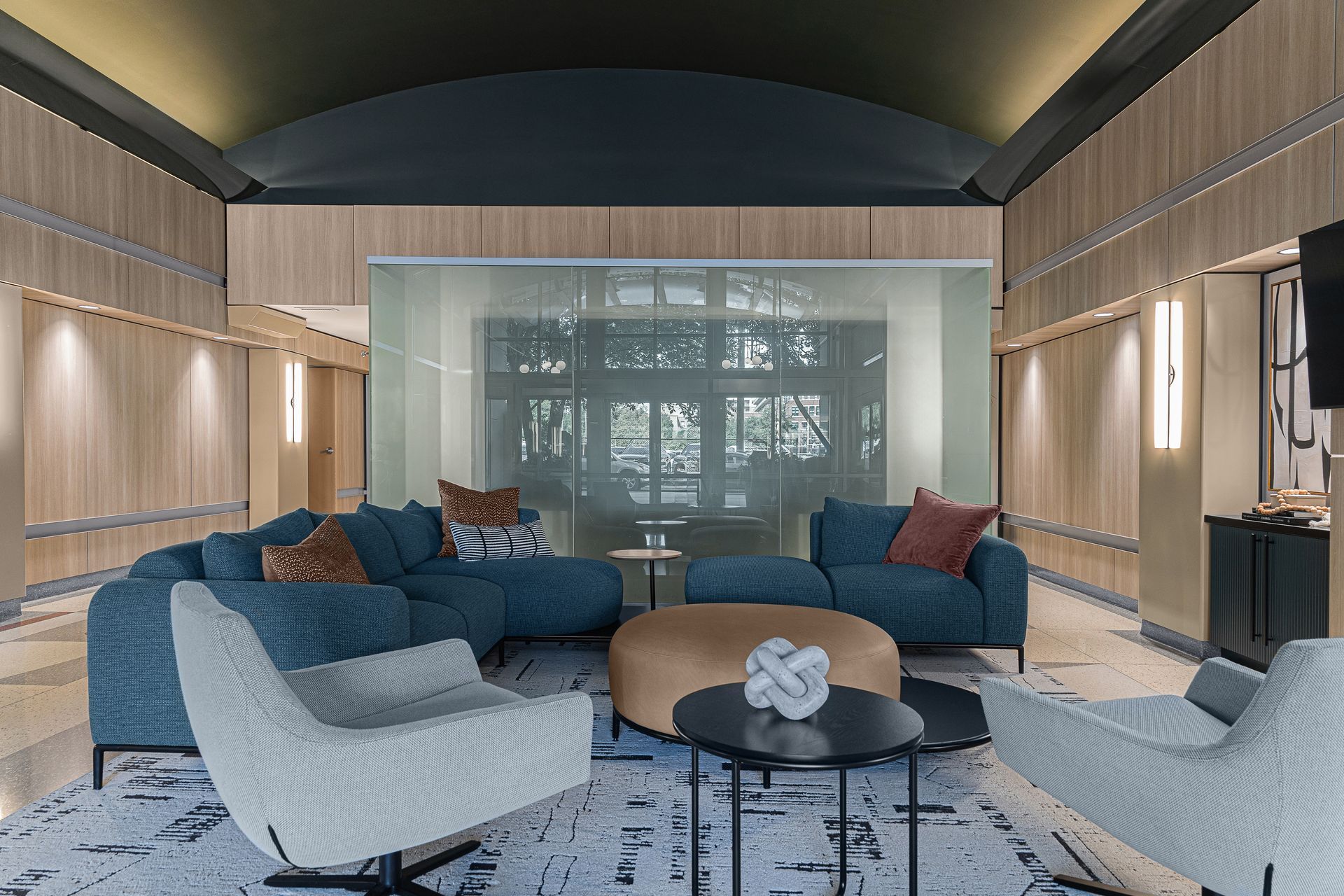 Modern living room with blue sectional sofa, light wood paneling, and large window view.