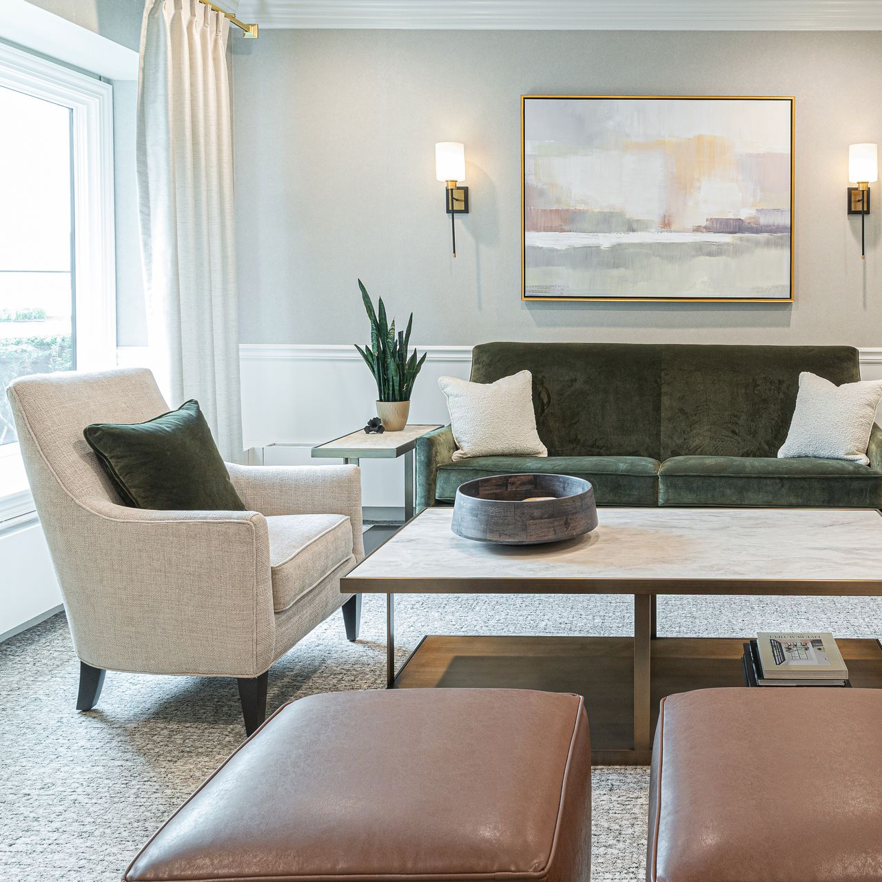Living room: Green velvet sofa, beige armchair, marble coffee table, artwork, and two ottomans.