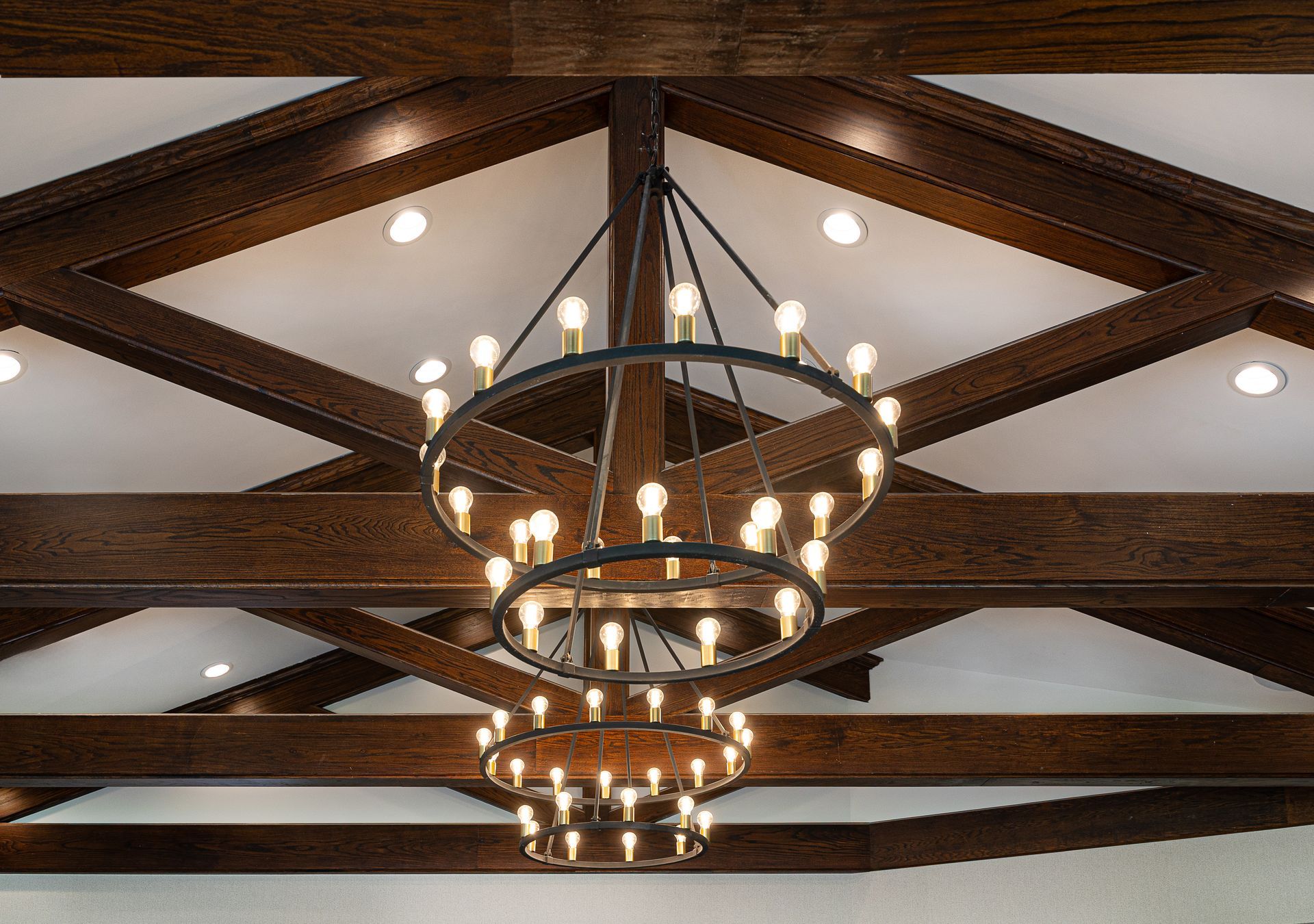 Dark wood beams and tiered chandelier in a white ceiling with recessed lights.