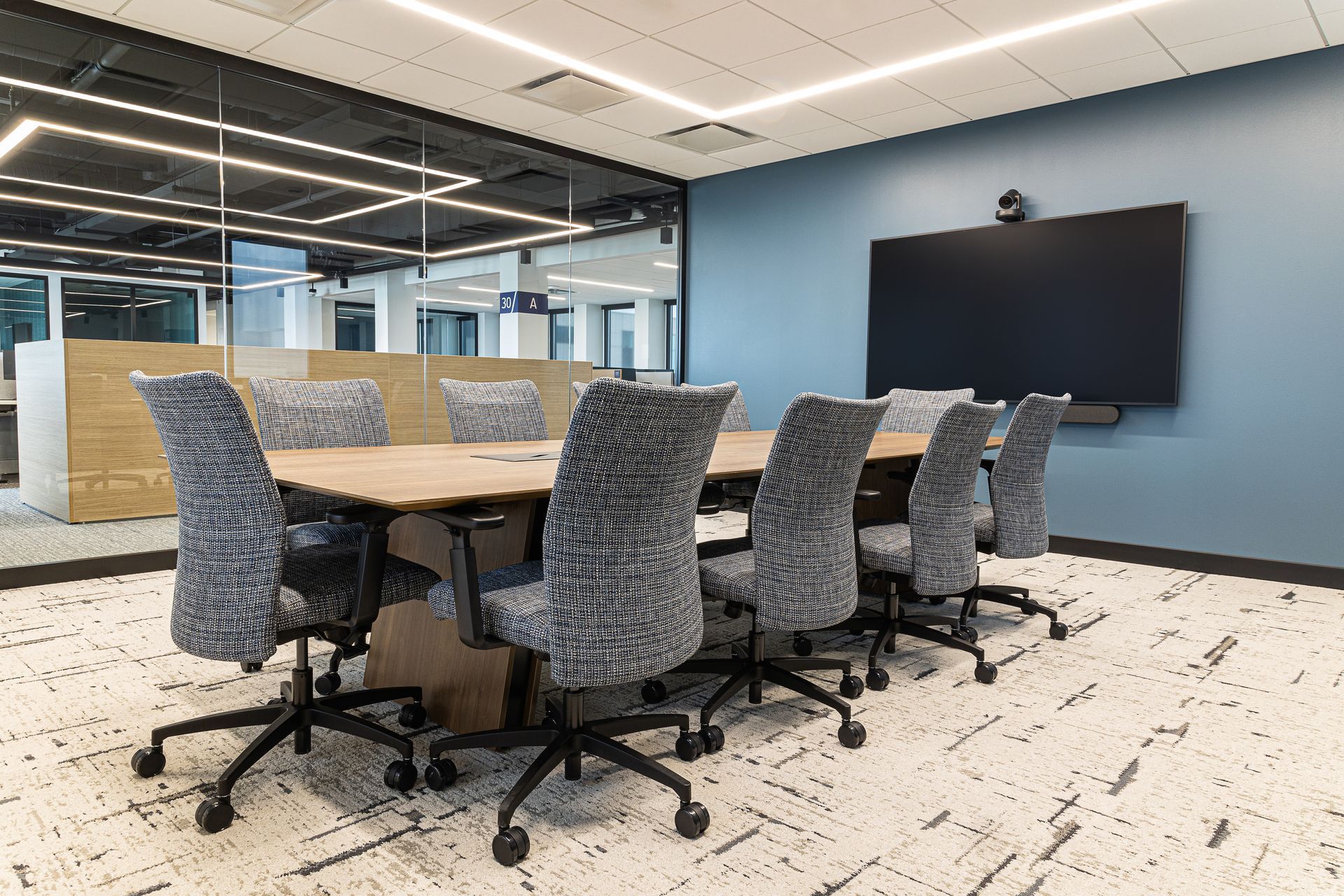 Conference room with a rectangular table, several chairs, and a large screen on a blue wall.