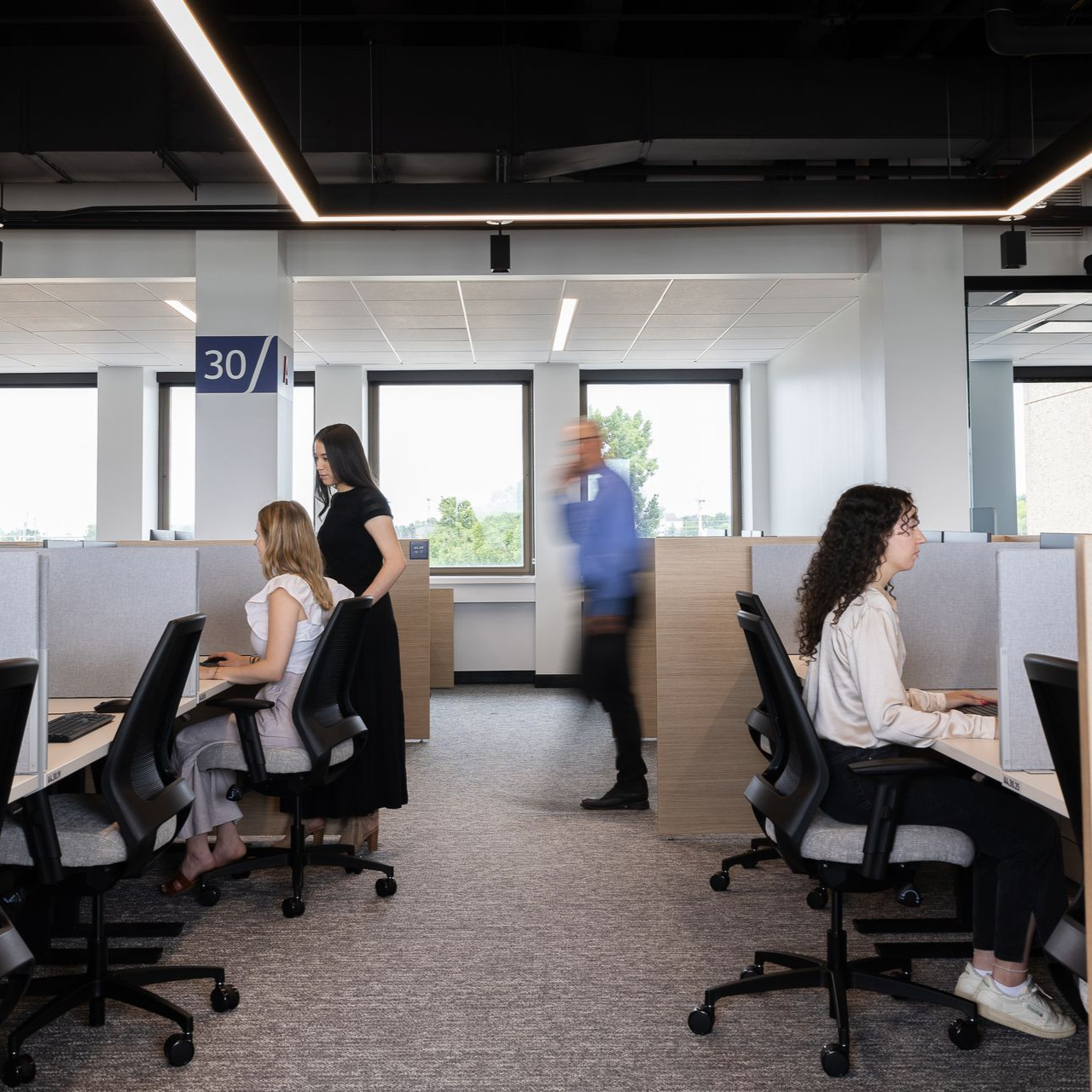 Office space with people at desks, one talking on the phone, others working. Bright lighting.