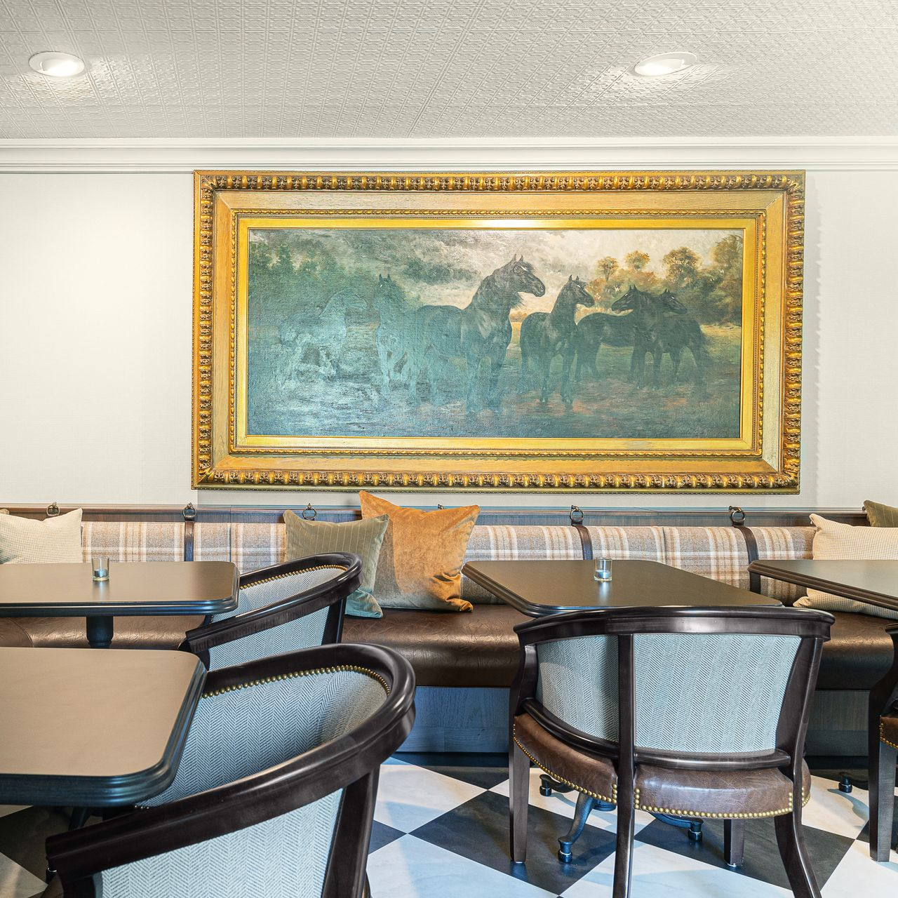 Restaurant dining area with brown booth seating, chairs, and horse painting. Black and white checkered floor.