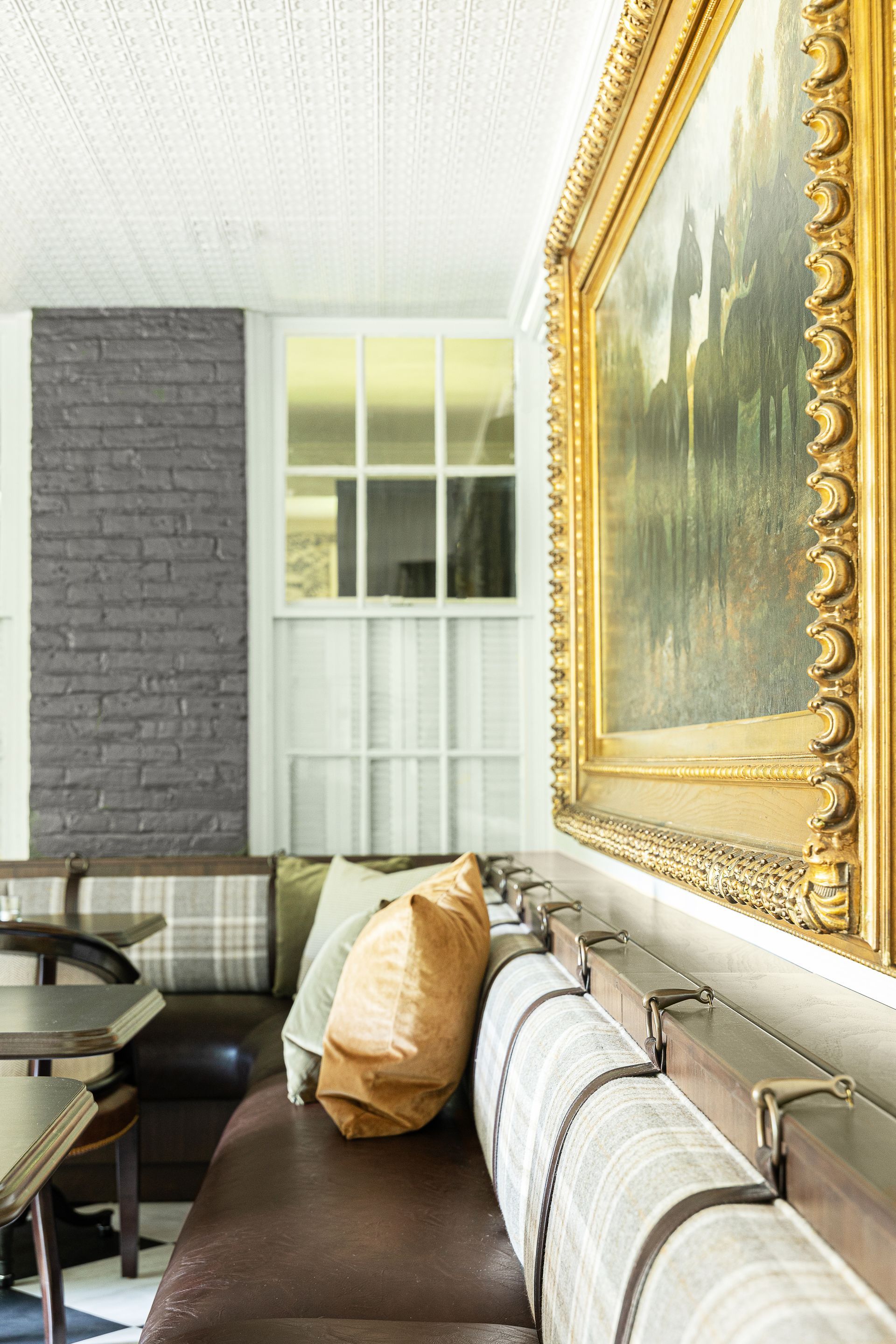 Cozy booth seating in a restaurant, featuring a leather bench, patterned pillows, and a large framed painting.