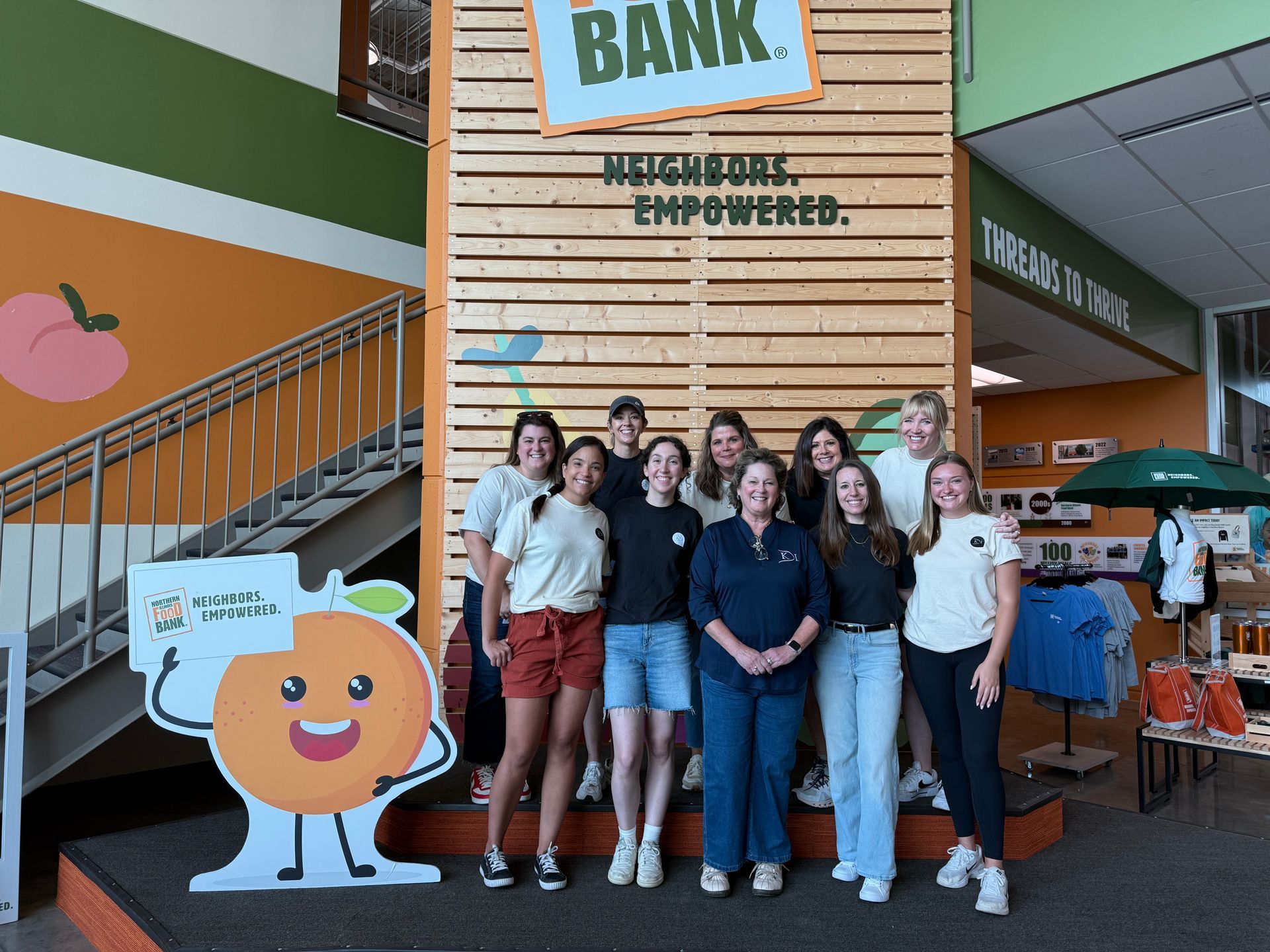 Group of people posing near a food bank sign; oranges and other produce displayed nearby.