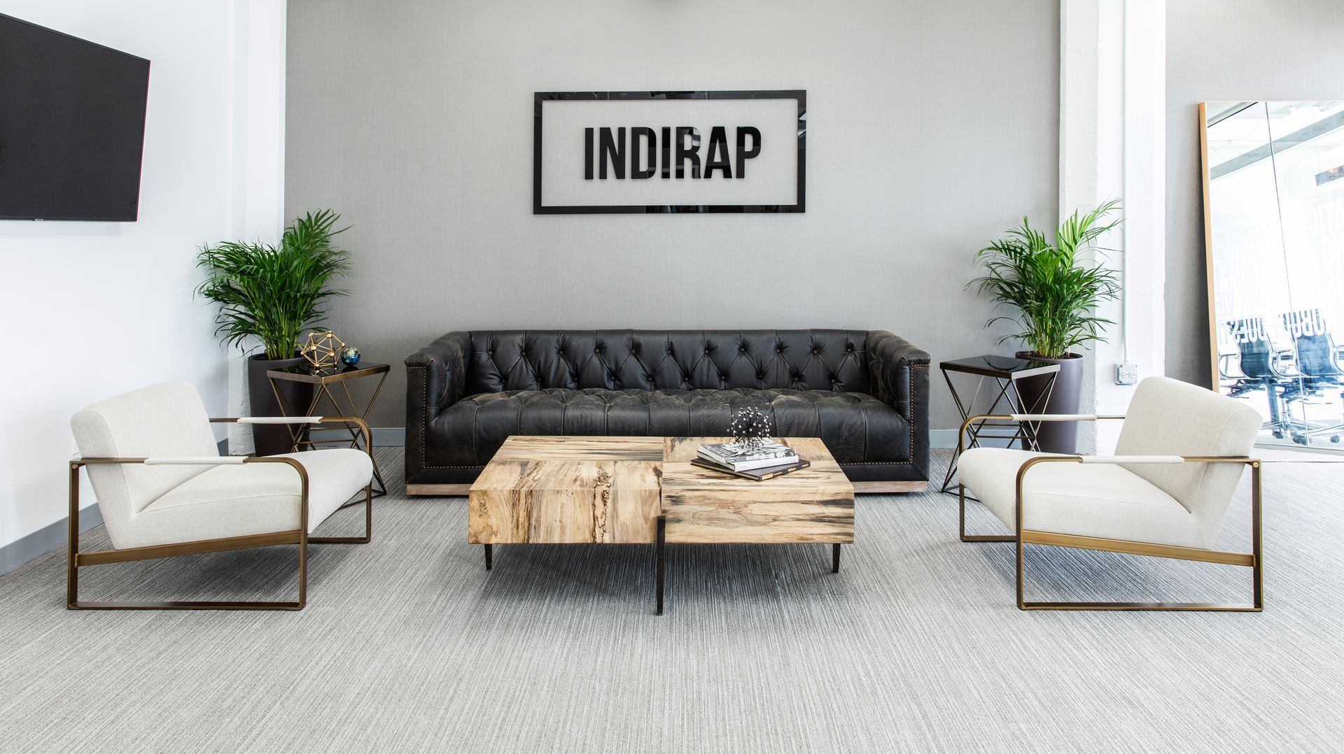 Lounge area with black leather sofa, two white armchairs, wooden coffee table, plants, and 