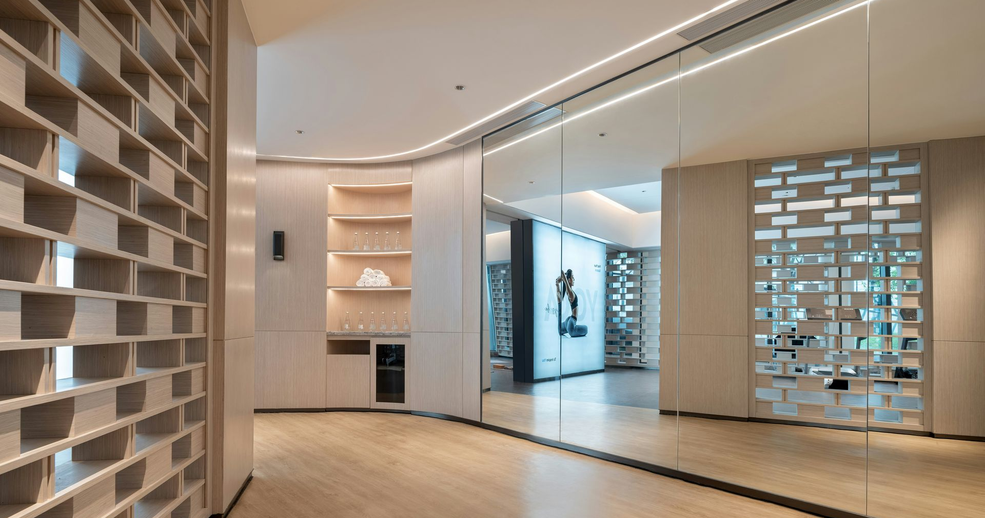 A minimalist room featuring light wood flooring, a decorative grid wall, built-in shelving, and a large wall mirror.
