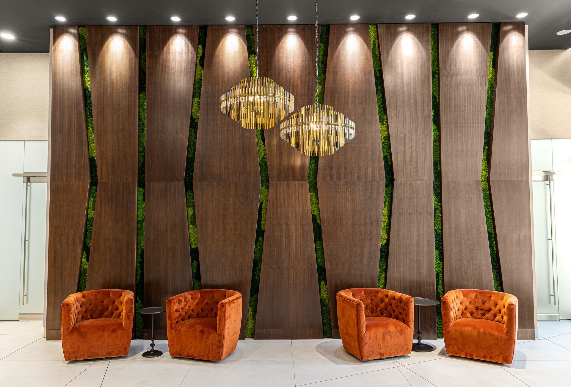 Lounge area with orange velvet chairs, wooden panel wall with green moss strips, and gold pendant lights.