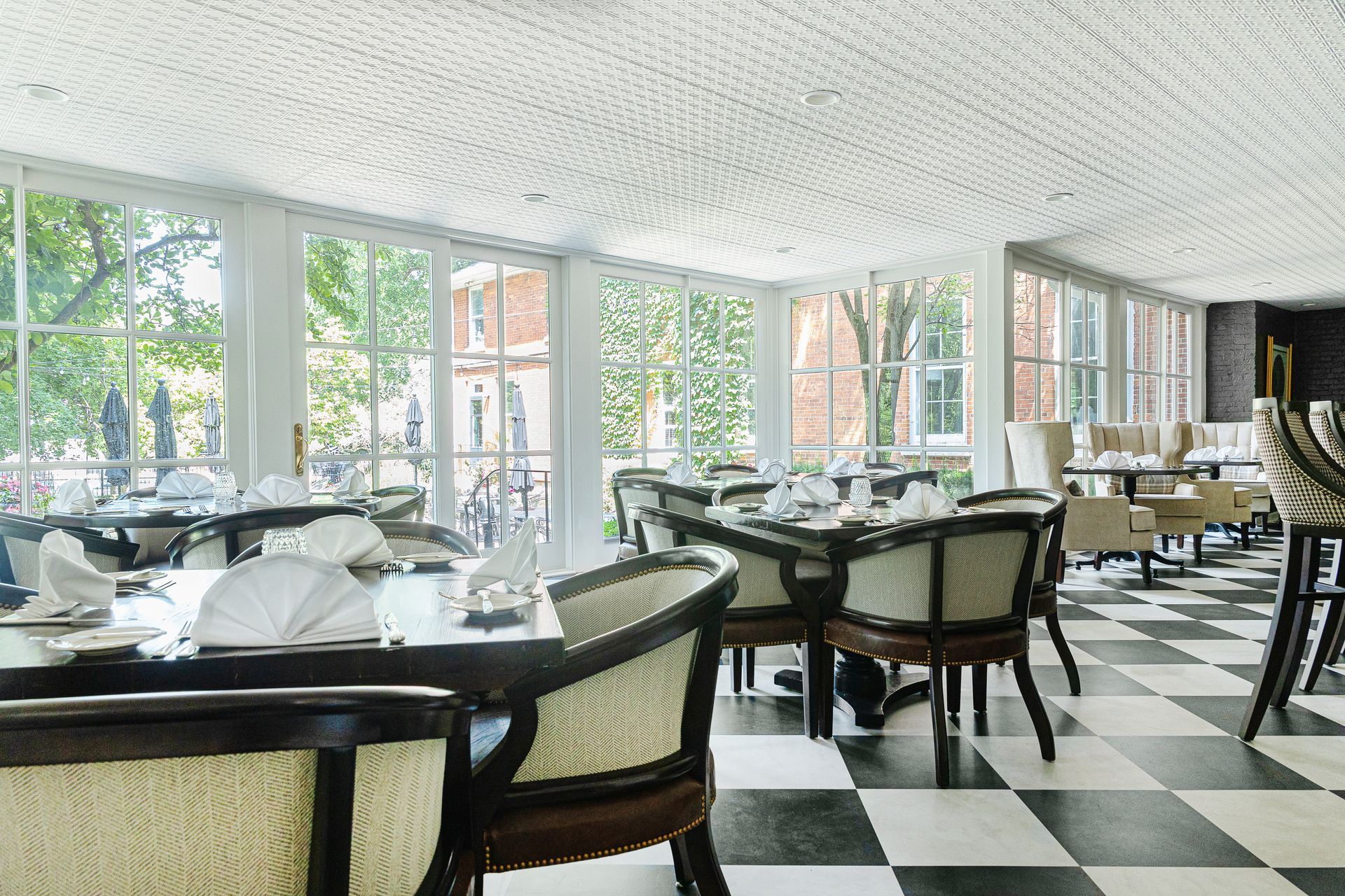 Restaurant dining room with tables set for service, checkerboard floor, and large windows.