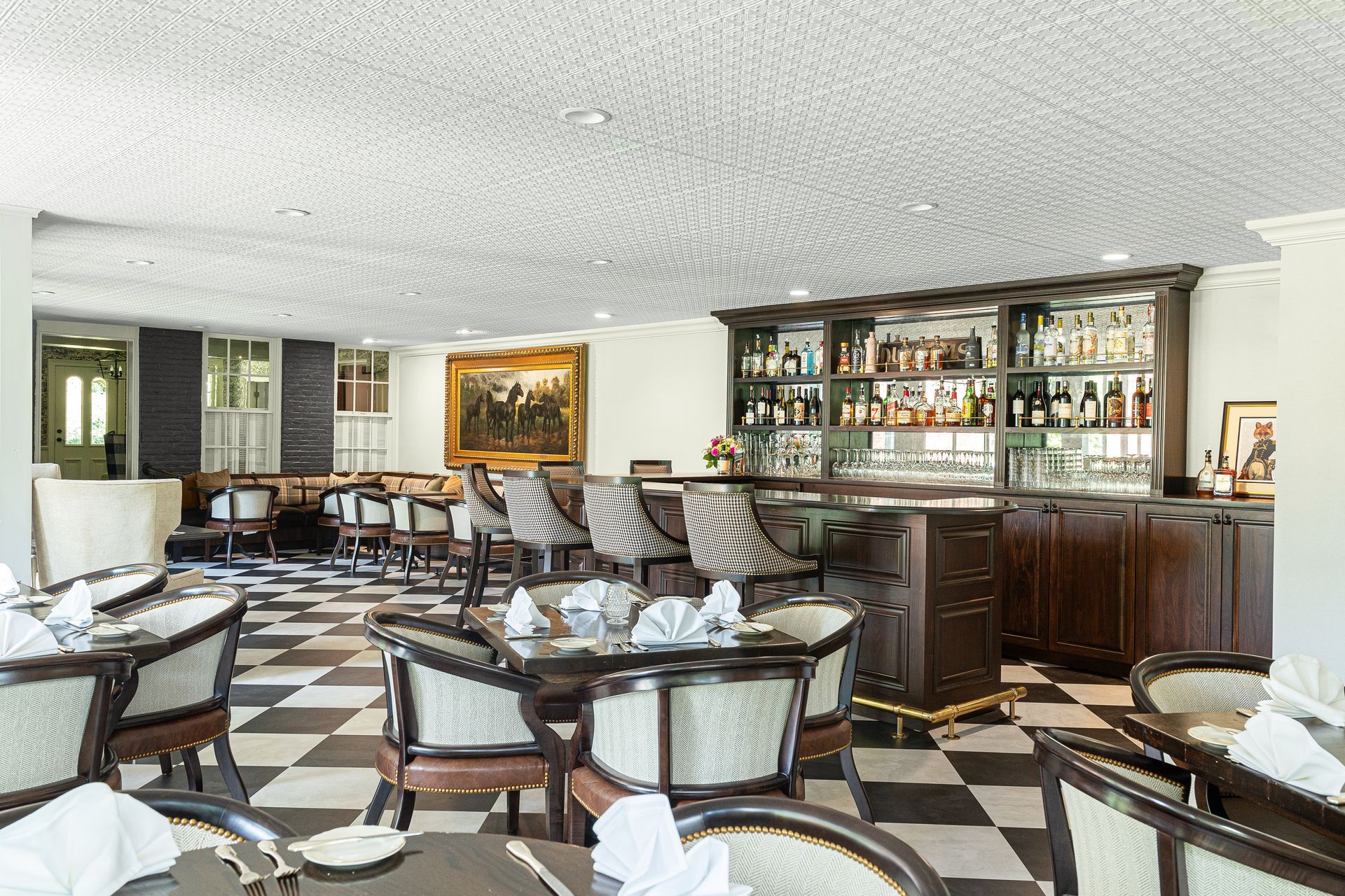 Restaurant interior with bar and dining tables on a checkered floor, adorned with classical paintings and dark wood.